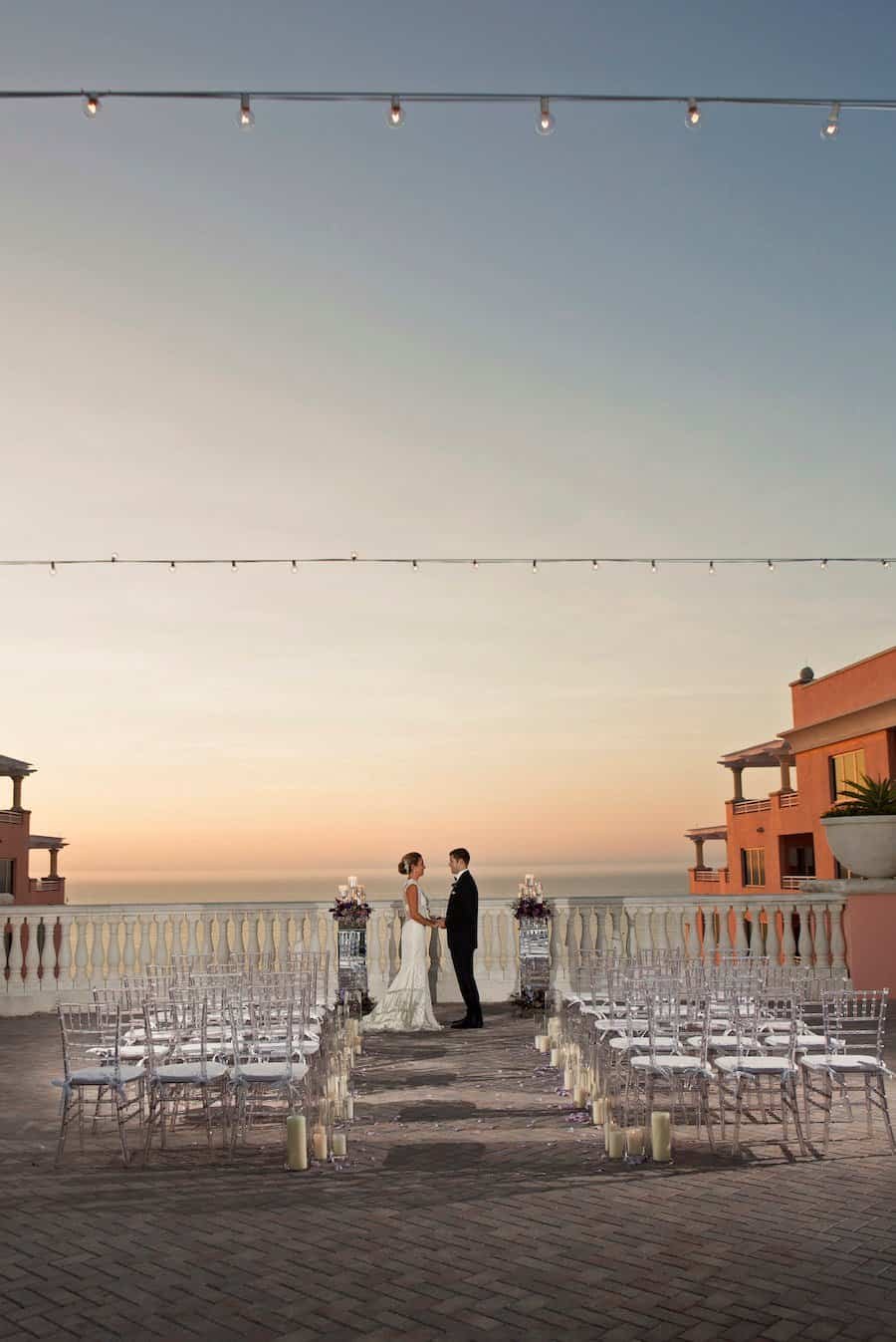 Sunset rooftop ceremony aisle lined with purple rose petals, candle lanterns, and clear Chiavari chairs at Hyatt Regency Clearwater Beach