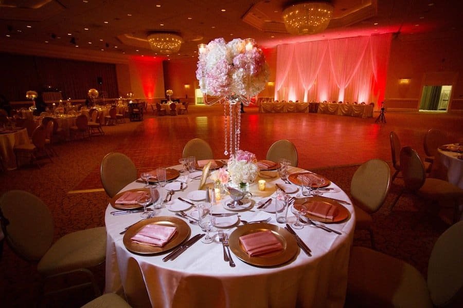 Reception dining tables featuring elevated floral centerpieces of coral hydrangeas, roses, and gold Chiavari chair seating