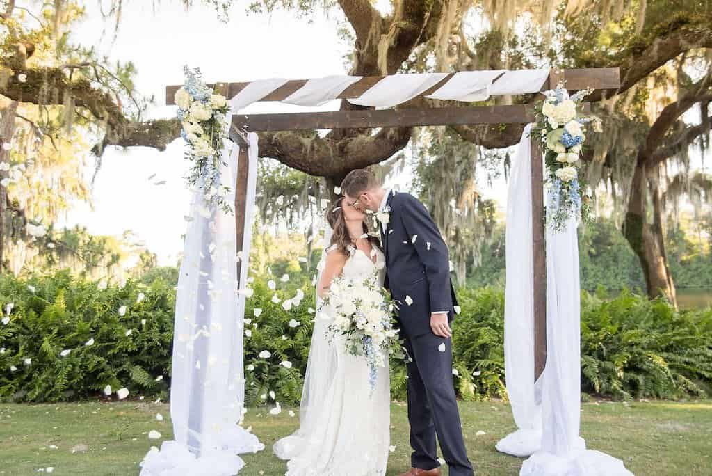 Palm Harbor Wedding Ceremony First Kiss Under Gabro Event Services Wooden Arch with White Draping and Floral Bouquets