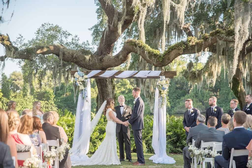 Bride and Groom Exchanging Wedding Vows Under Custom Wooden Arch with White Draping on the Golf Course at Innisbrook Resort