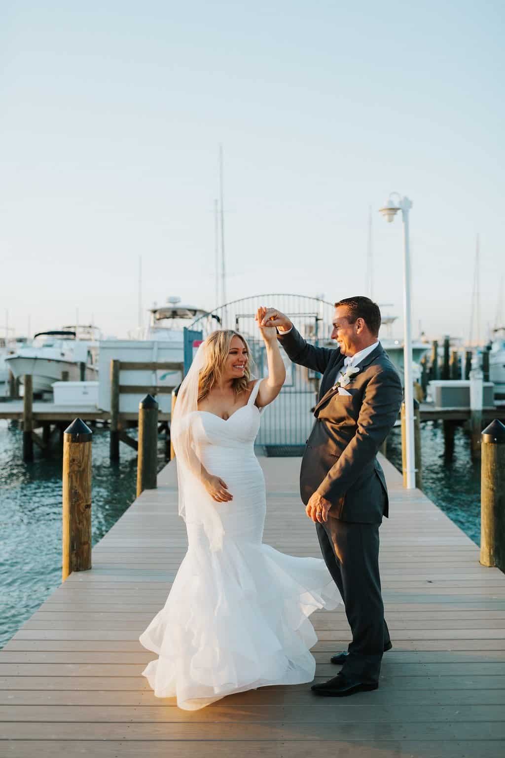 Bride in lace gown and groom in grey tuxedo holding hands on the waterfront dock at Isla Del Sol