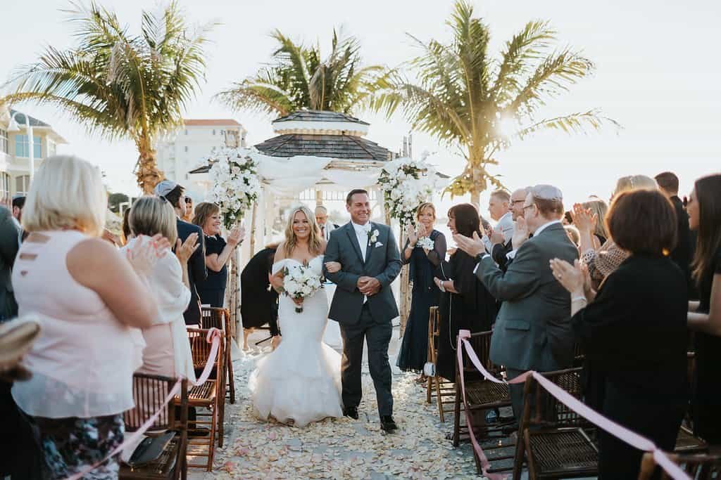 A reception ballroom featuring clear chairs and white floral centerpieces on tables.