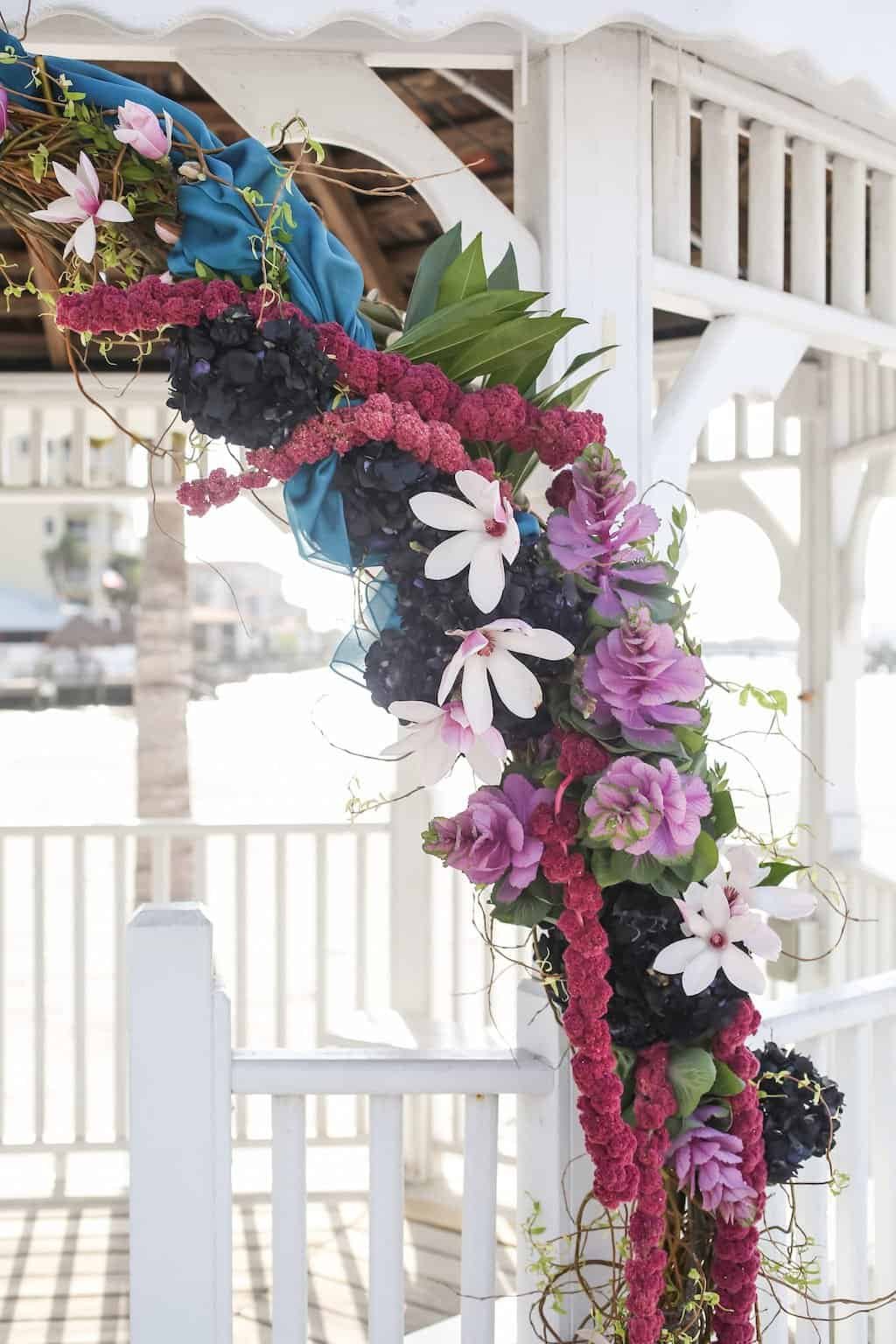 Waterfront wedding ceremony altar at Isla Del Sol Yacht Club featuring rich plum and magenta florals with cascading sheer draping