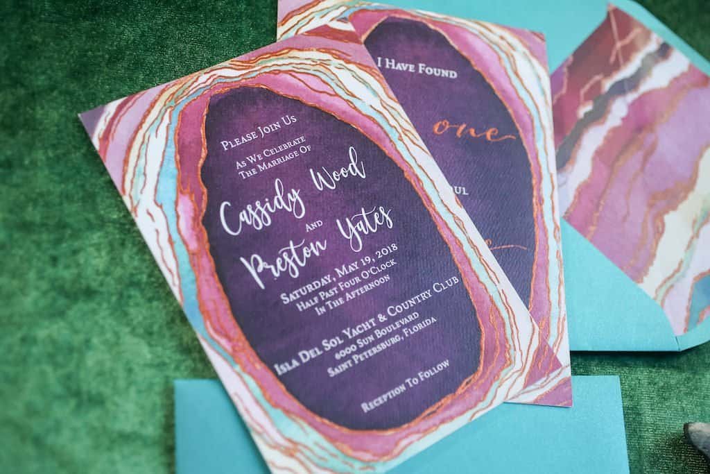 Modern geode-themed wedding reception table with plum linens, copper chargers, and vibrant jewel-toned floral centerpiece