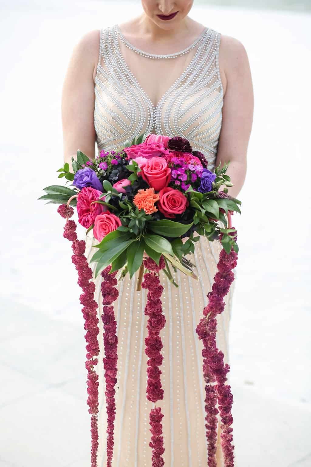 A circular wedding arbor adorned with plum and fuchsia flowers by the water.