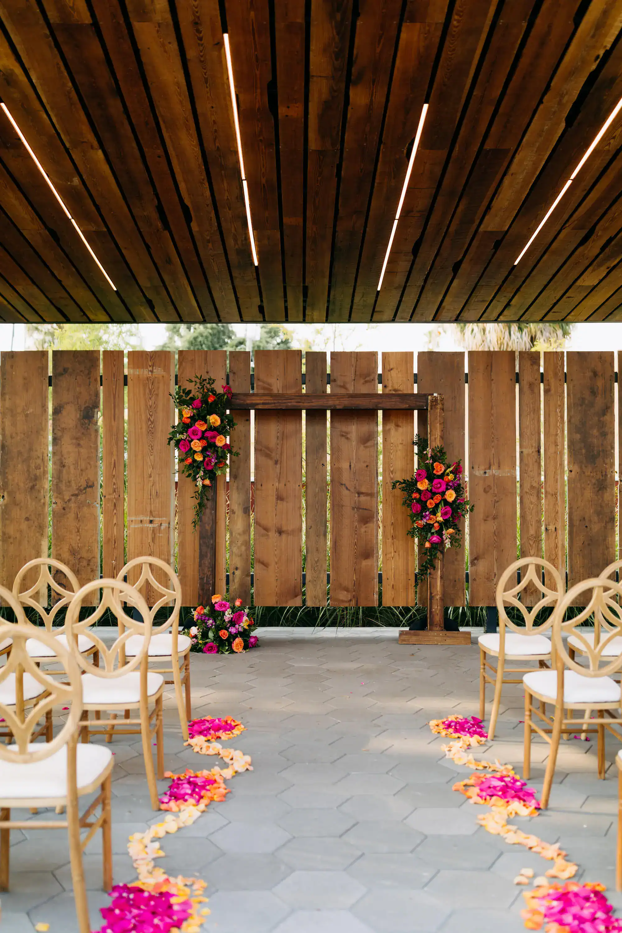 Wooden ceremony arch with pink and orange roses, greenery, and Ybor red brick factory backdrop