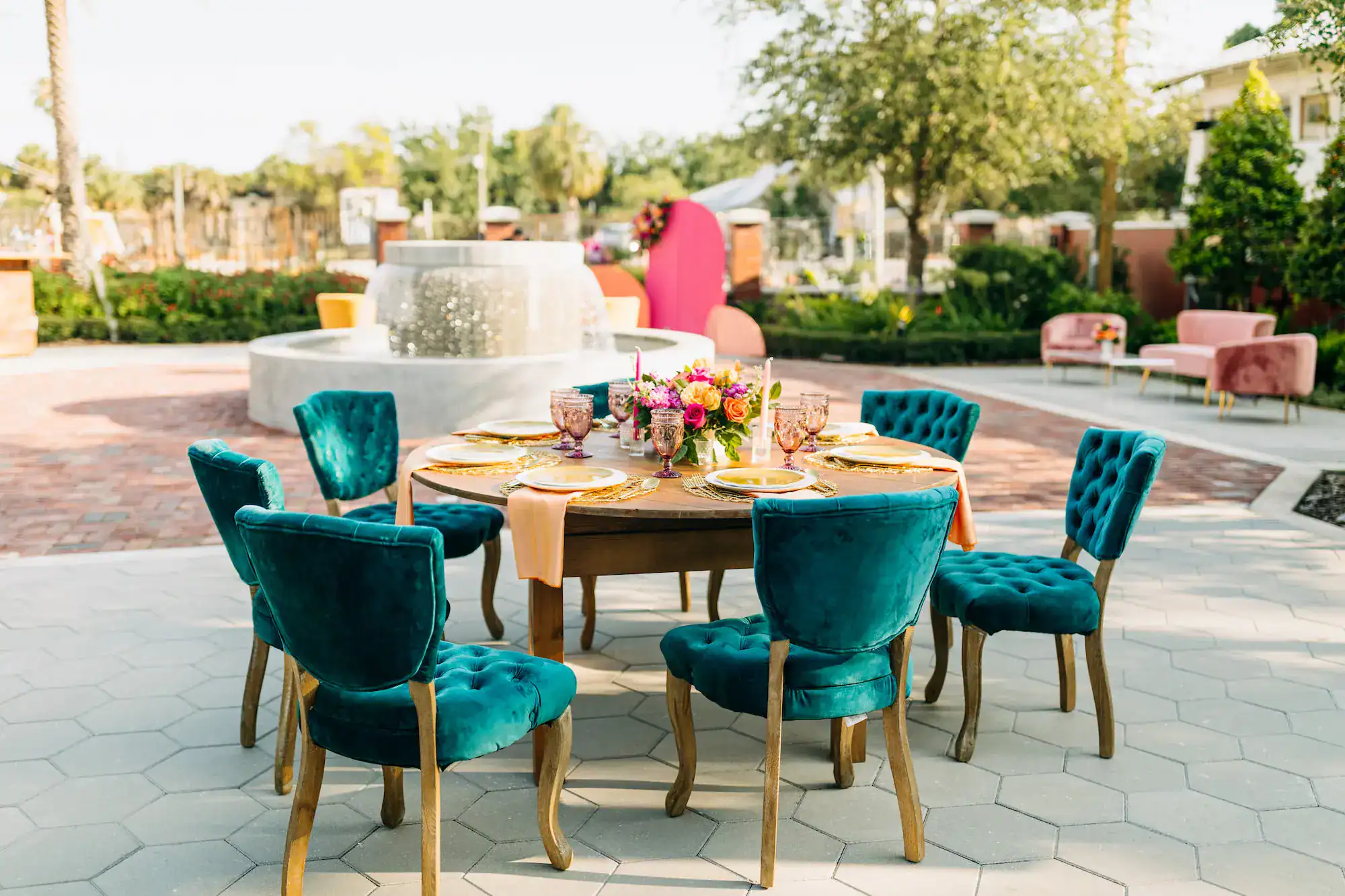 Vibrant summer wedding reception place setting with orange carnations, yellow tulips, pink roses, and blue velvet chairs from Gabro Event Services