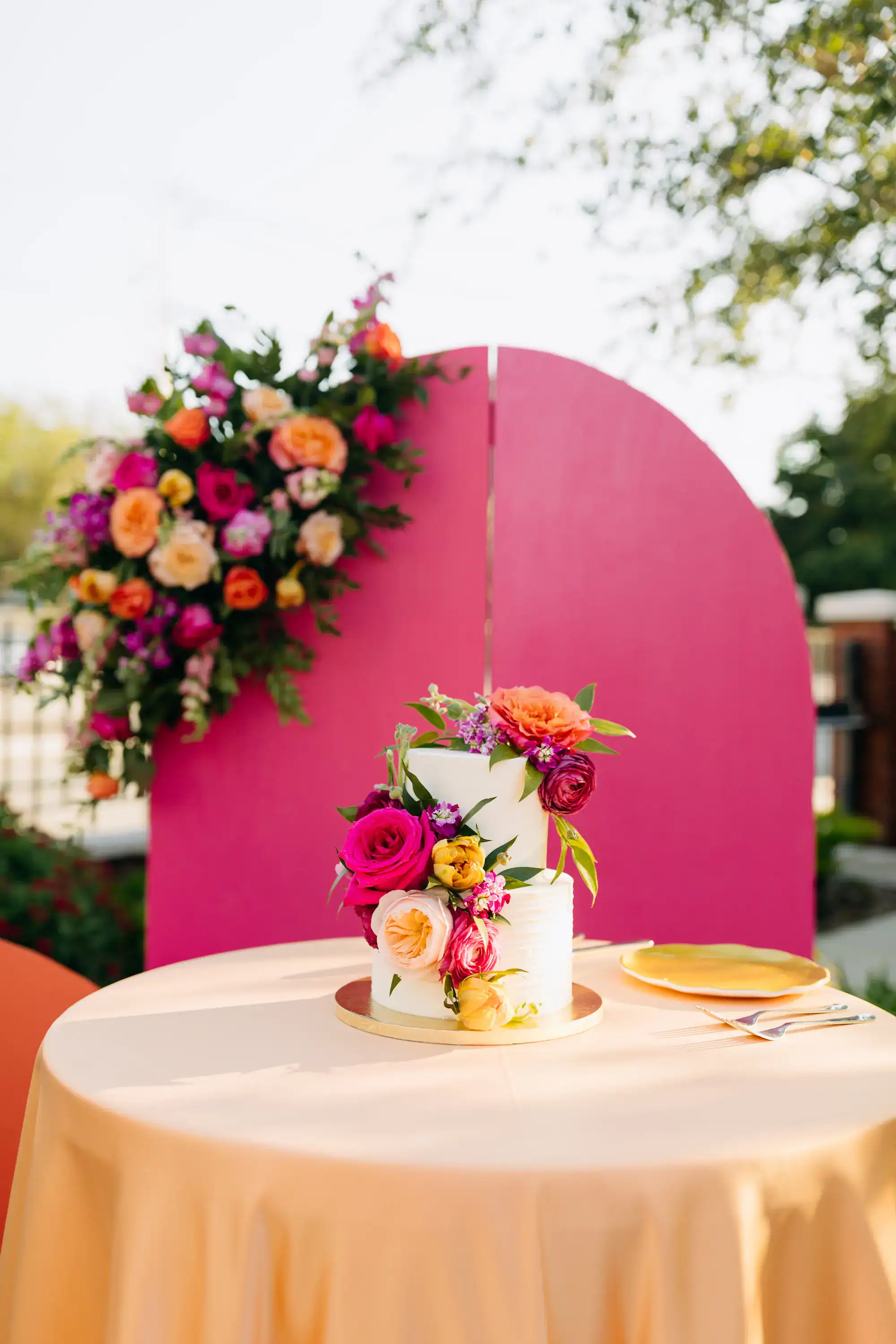 Vibrant summer wedding cake with fuchsia pink roses and orange tulips on pink arch backdrop