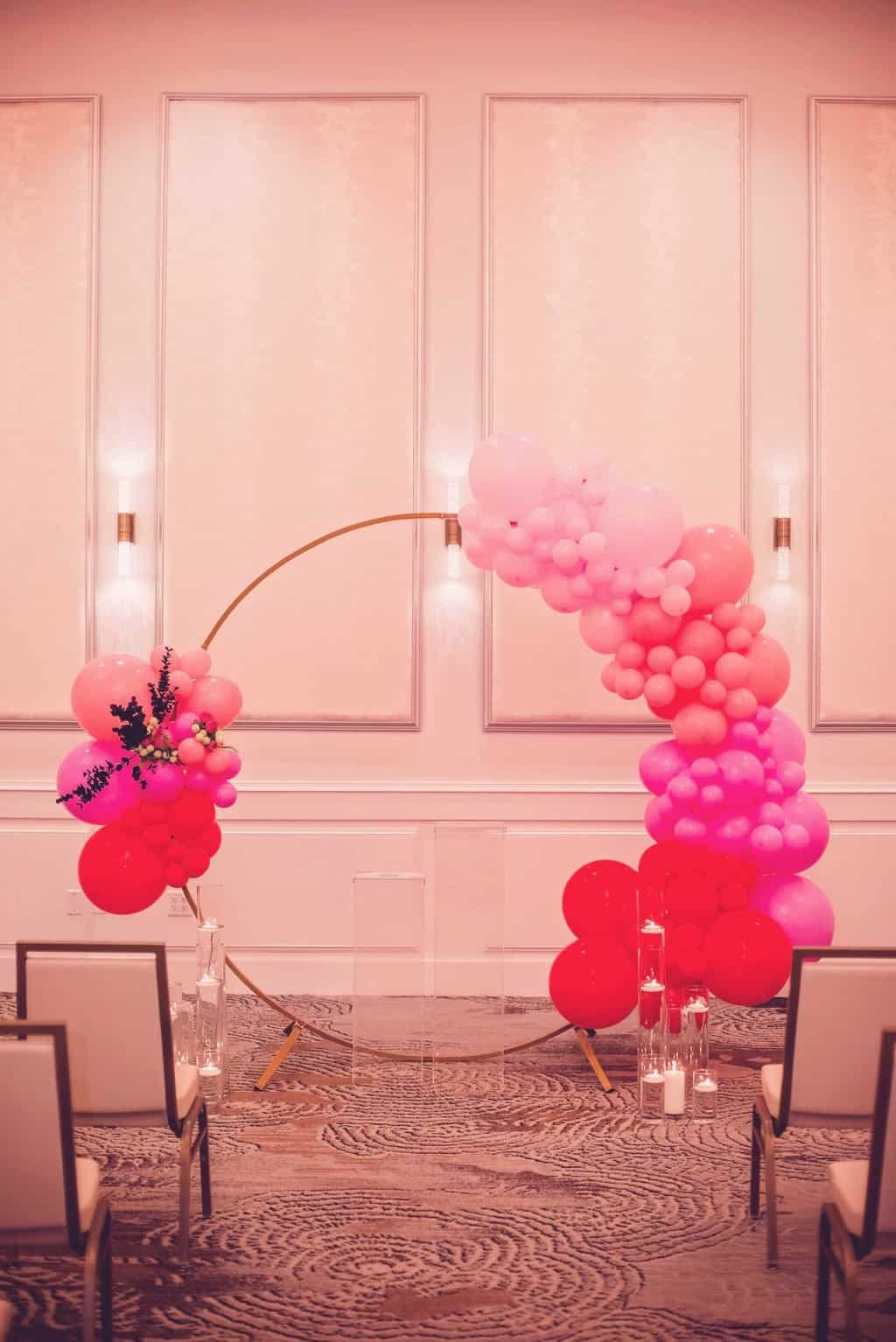 Modern Valentine wedding ceremony arch featuring cascading pink and red ombre balloon garland at The Karol Hotel
