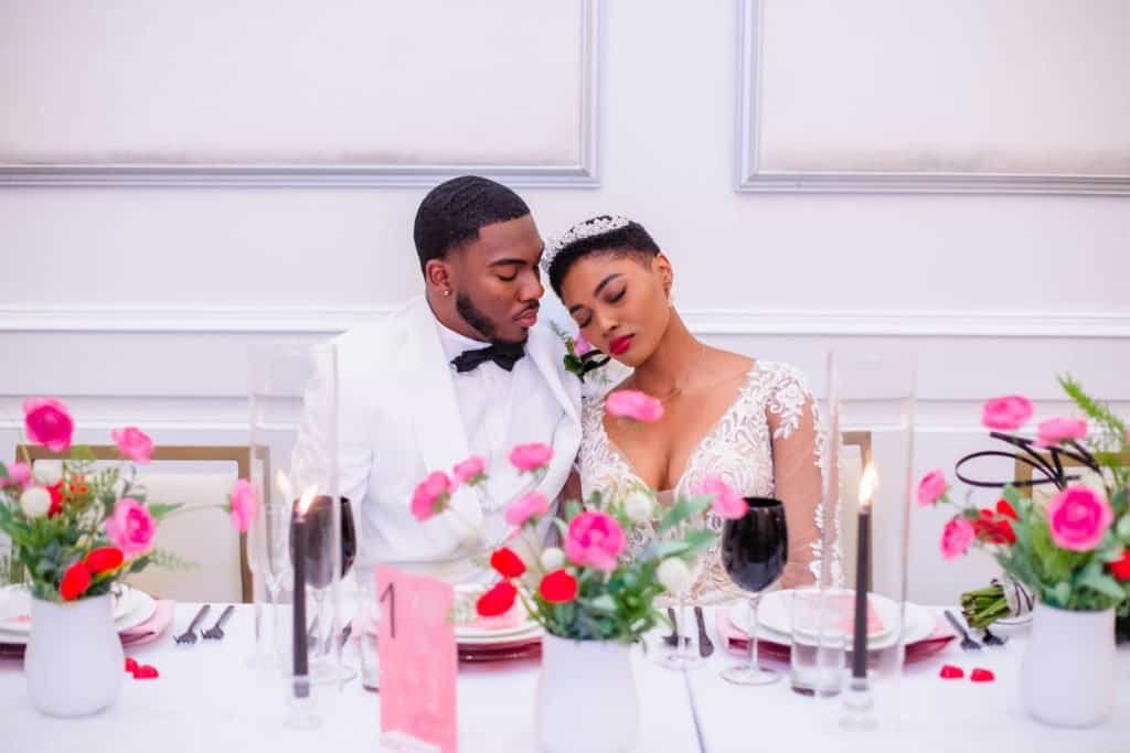 Bride and groom seated at romantic Valentine reception table with custom menu cards and red rose florals
