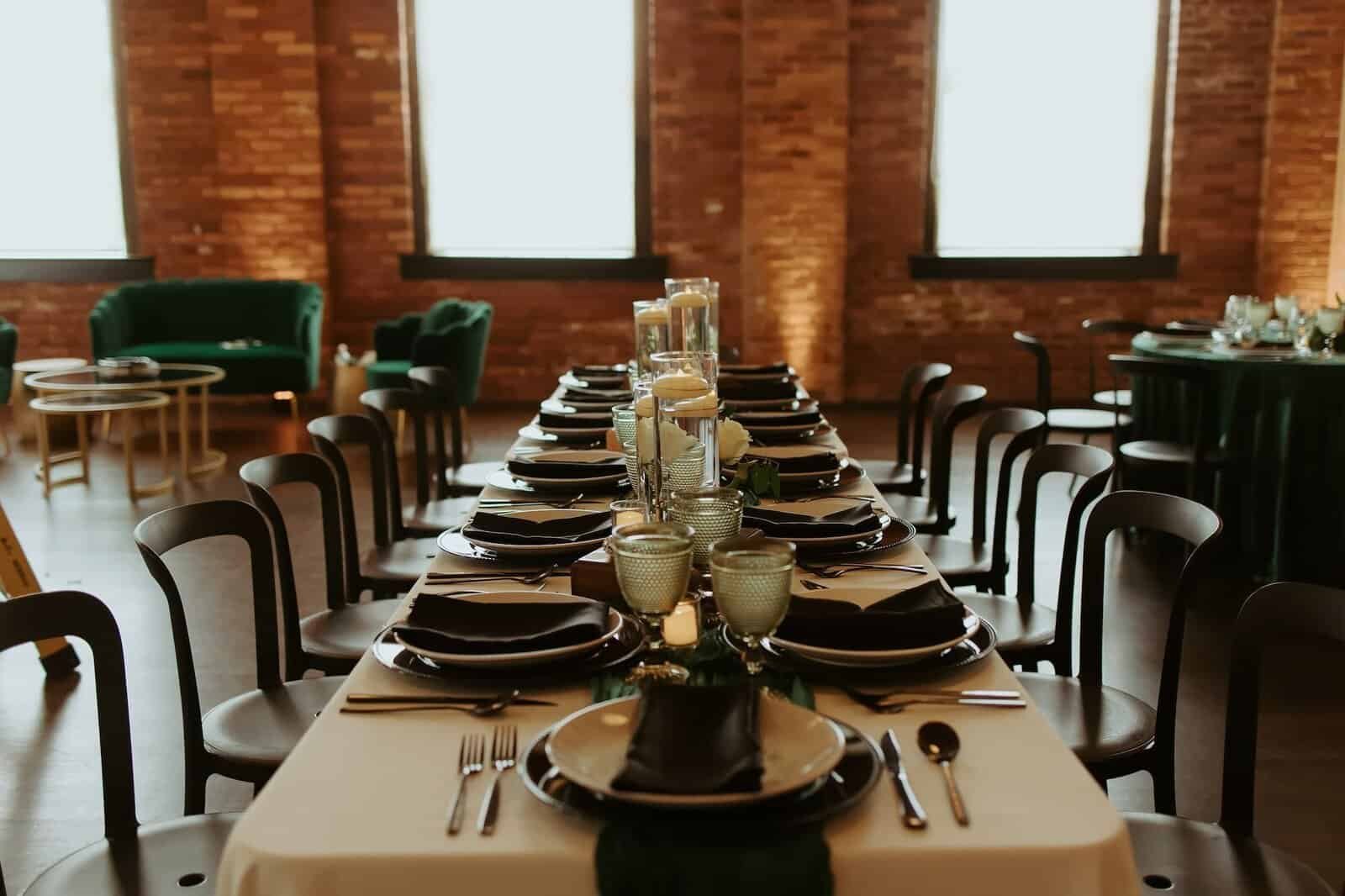 Long reception table with black chairs, dark chargers and candles running through the brick factory room