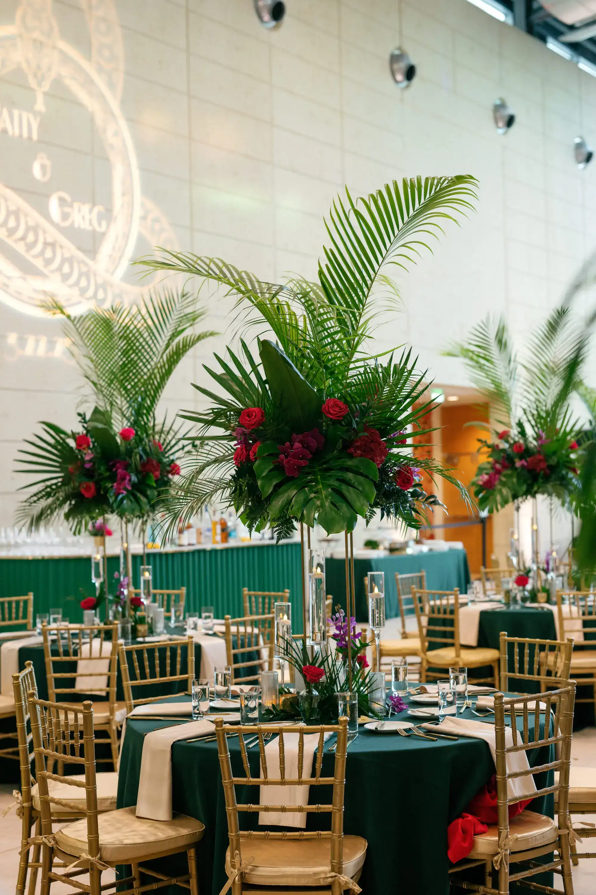 Reception tablescape details with gold charger plates, emerald velvet napkins, and tropical floral runners from Gabro Event Services