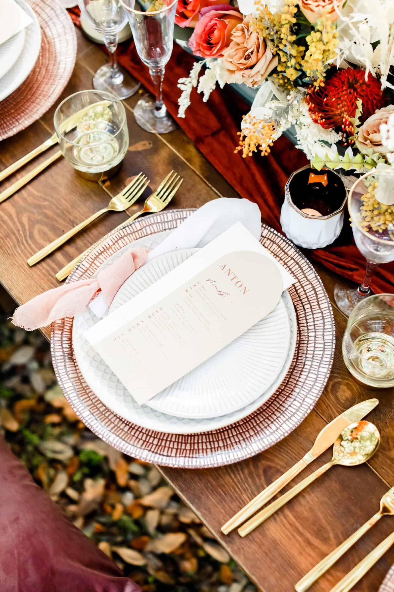 Place setting with brass flatware and dried florals on a bare wood table