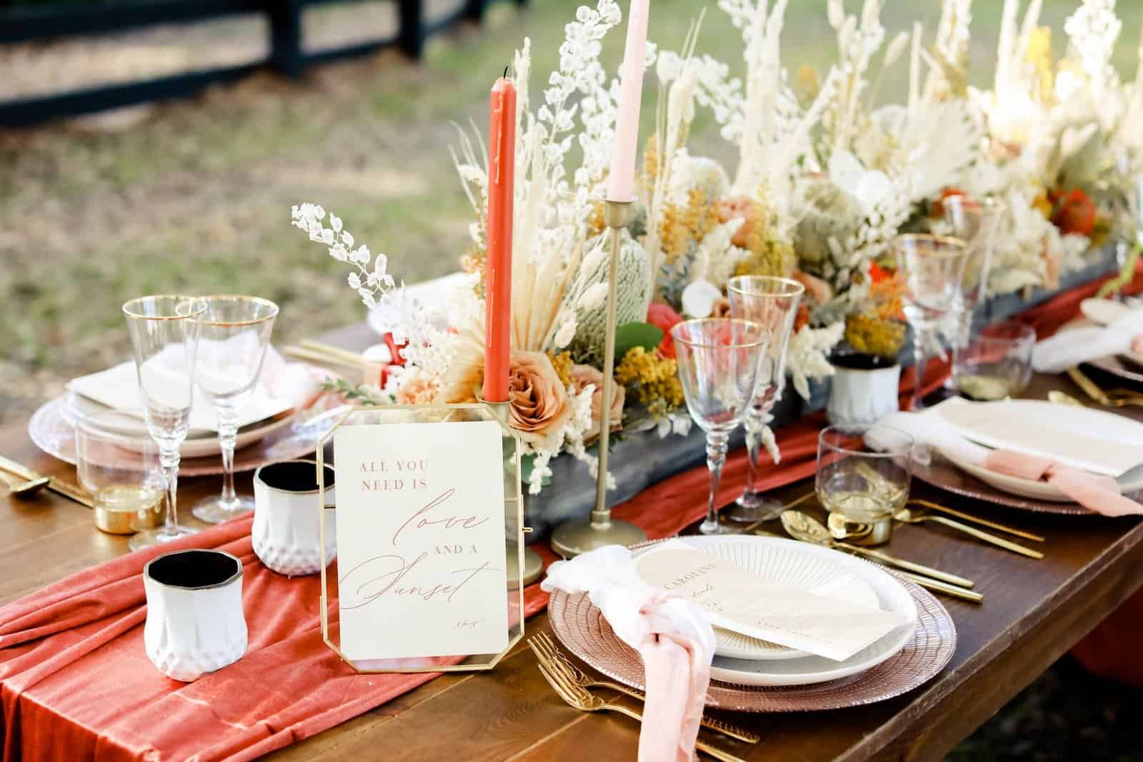 Terracotta gauze table runner with amber pillar candles and dried floral centerpieces on wooden farm table