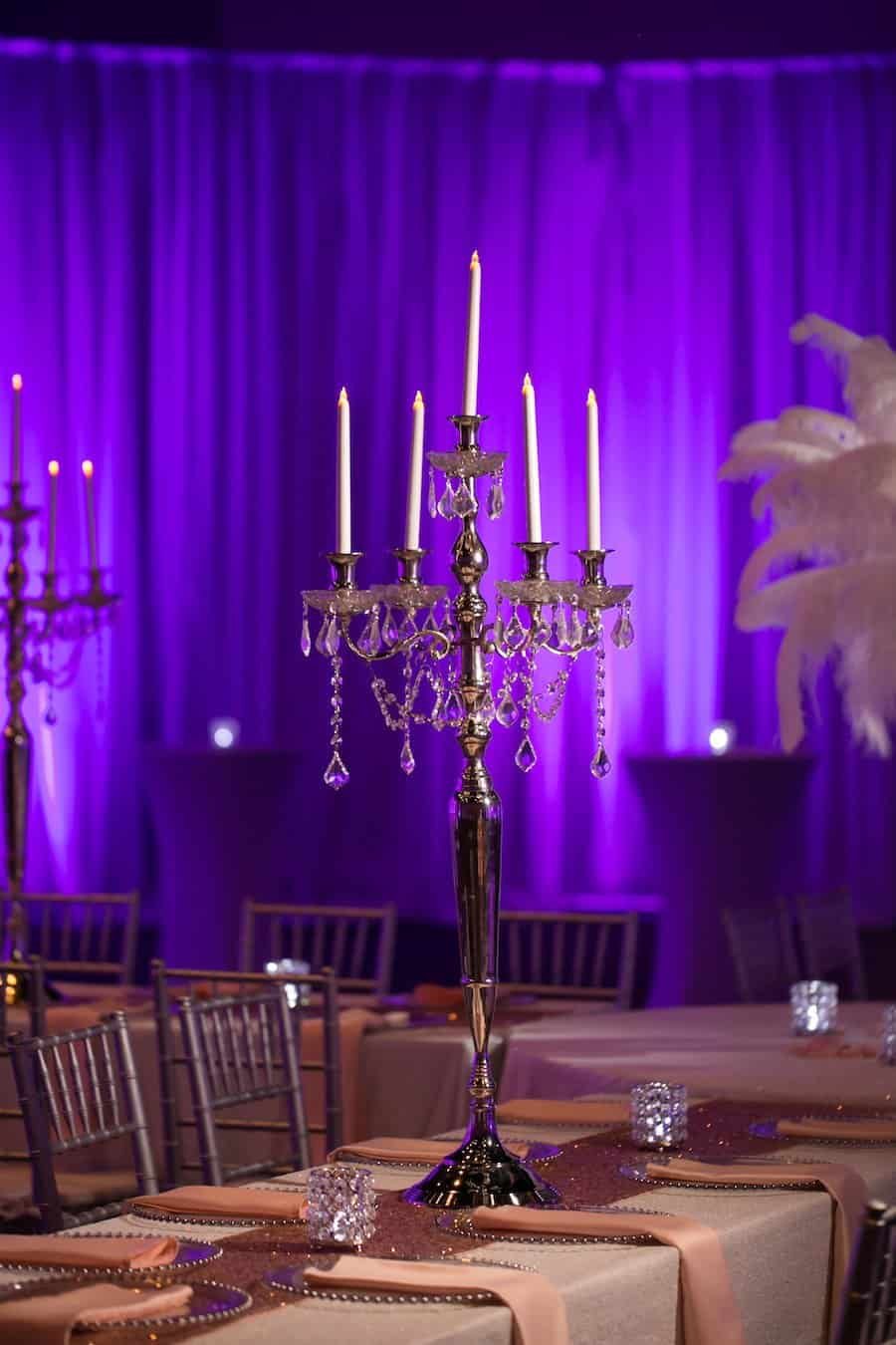 Luxury wedding table place setting with glass beaded charger plate, blush satin napkin, and towering crystal candelabra centerpiece
