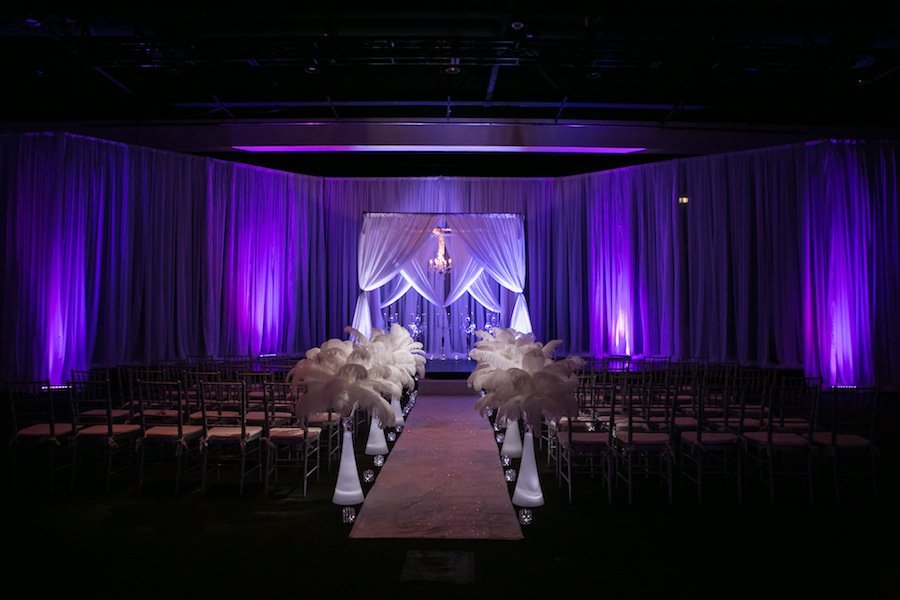 Modern angelic wedding ceremony aisle featuring Gabro Event Services white fabric canopy, silver Chiavari chairs, and feather aisle accents