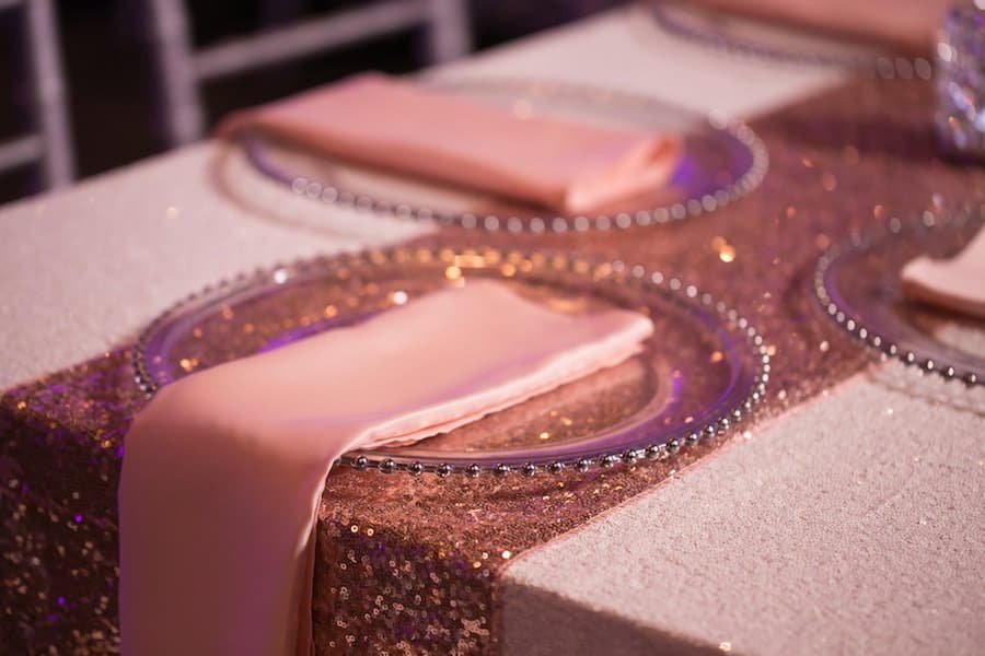 Refined wedding dining place setting featuring Gabro Event Services beaded glass charger and folded blush satin napkin
