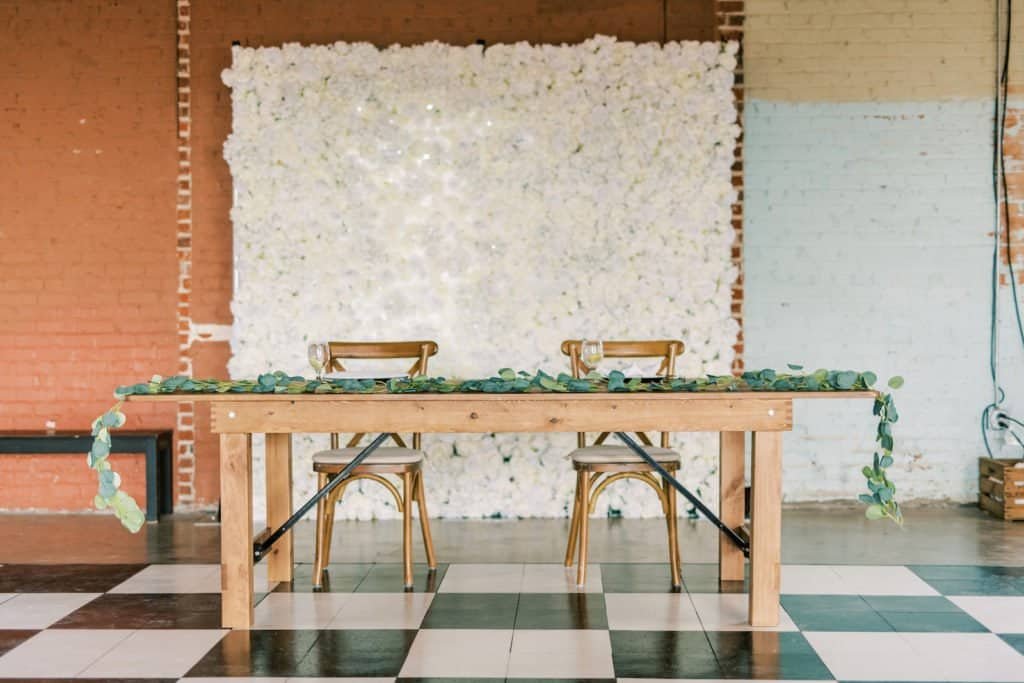 Farm table head table with cross-back chairs against brick wall at Morean Center for Clay
