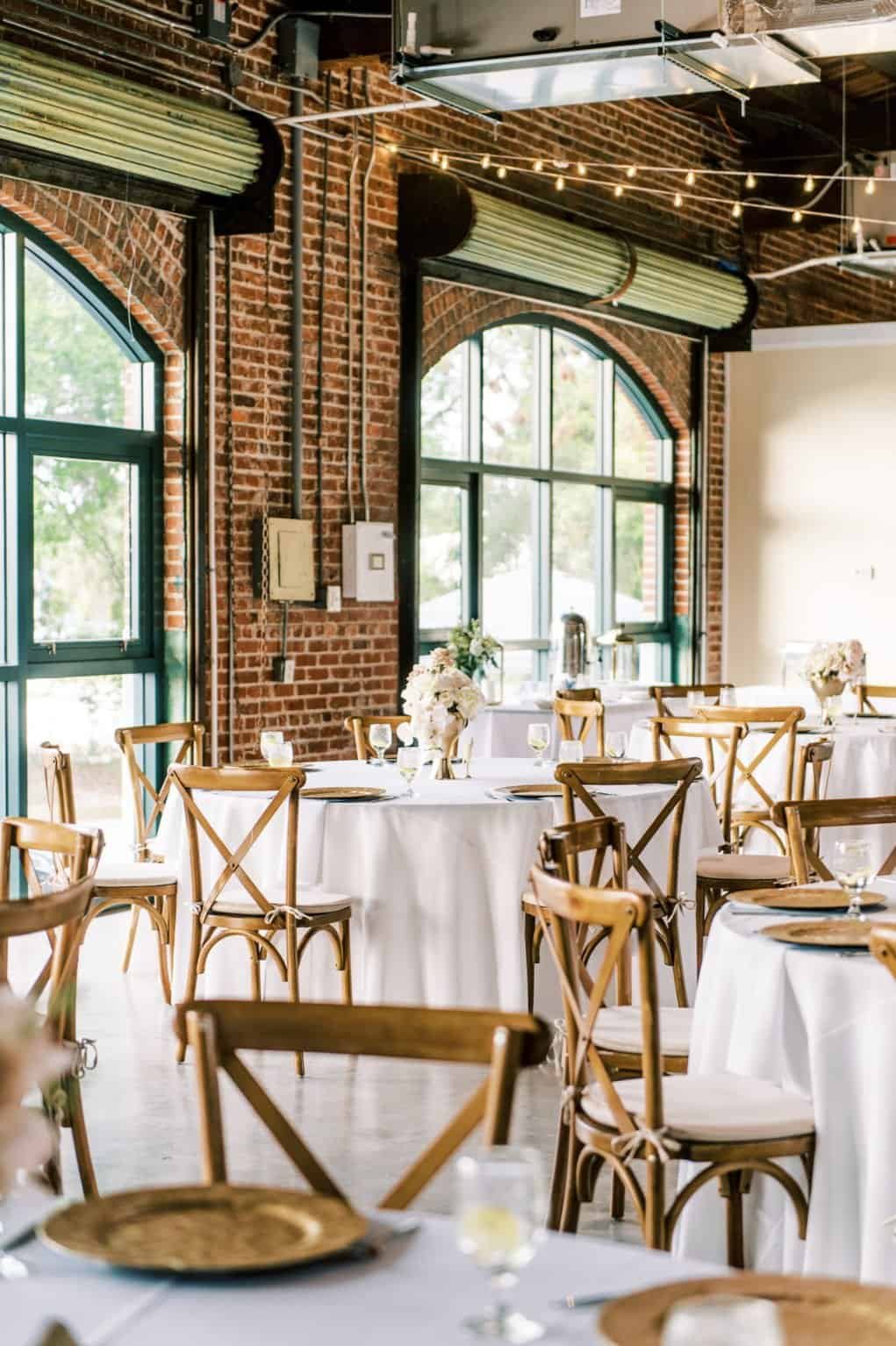 Reception at the Morean Center for Clay with round tables, cross-back chairs and string lights under a timber and brick ceiling