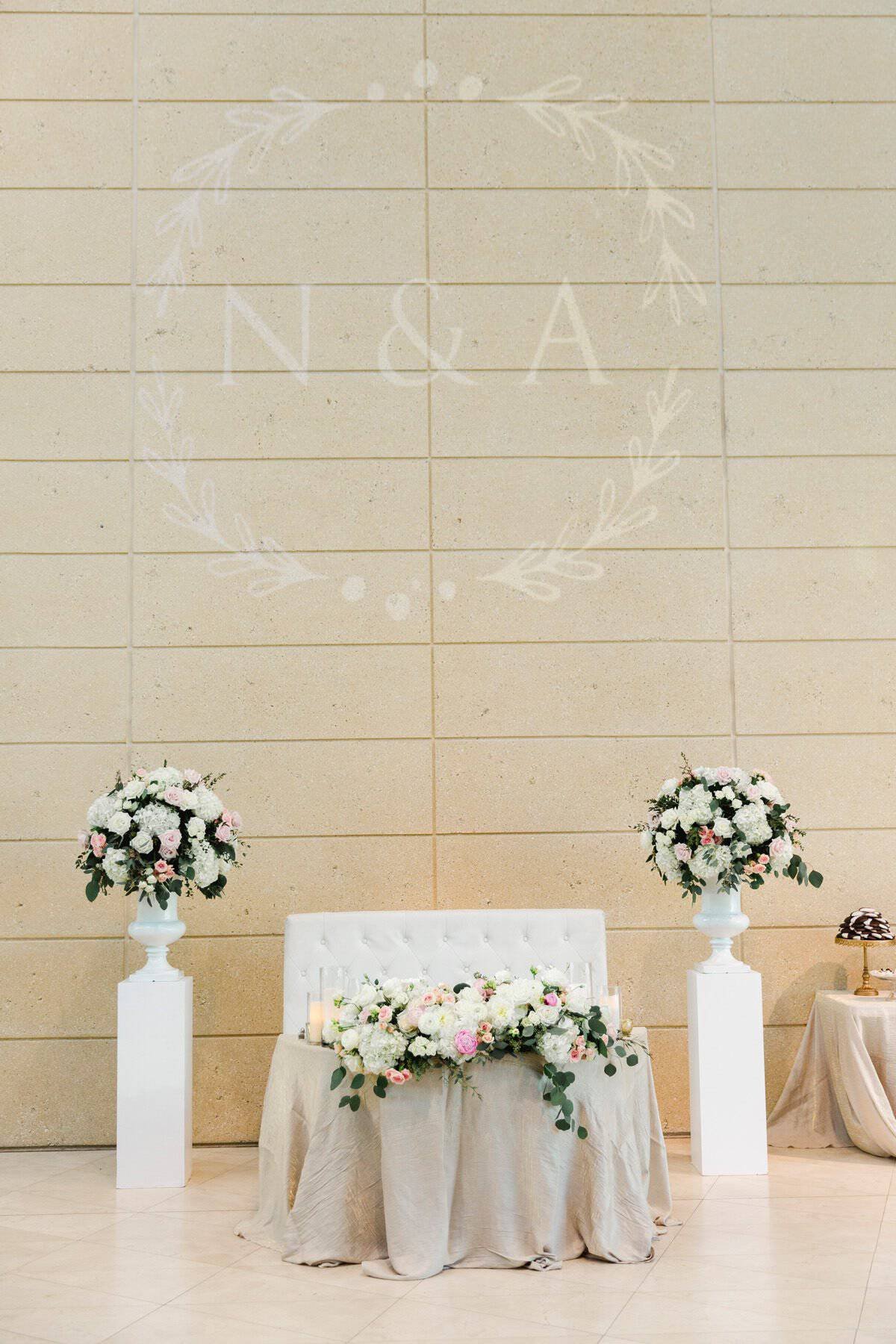 Nora and Adam's intimate sweetheart table setup with tufted loveseat, floral columns, and custom monogram gobo lighting by Gabro Event Services