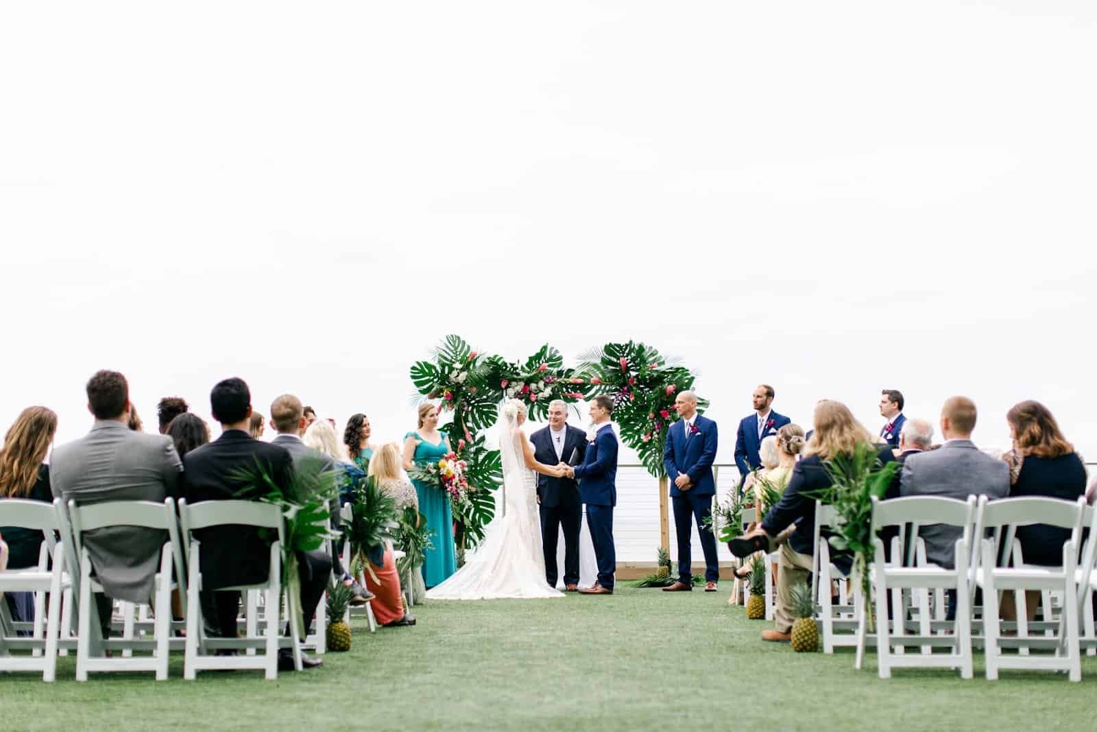 Bride and Groom Exchanging Wedding Vows Under Tropical Floral Arch on Clearwater Beach Waterfront Lawn