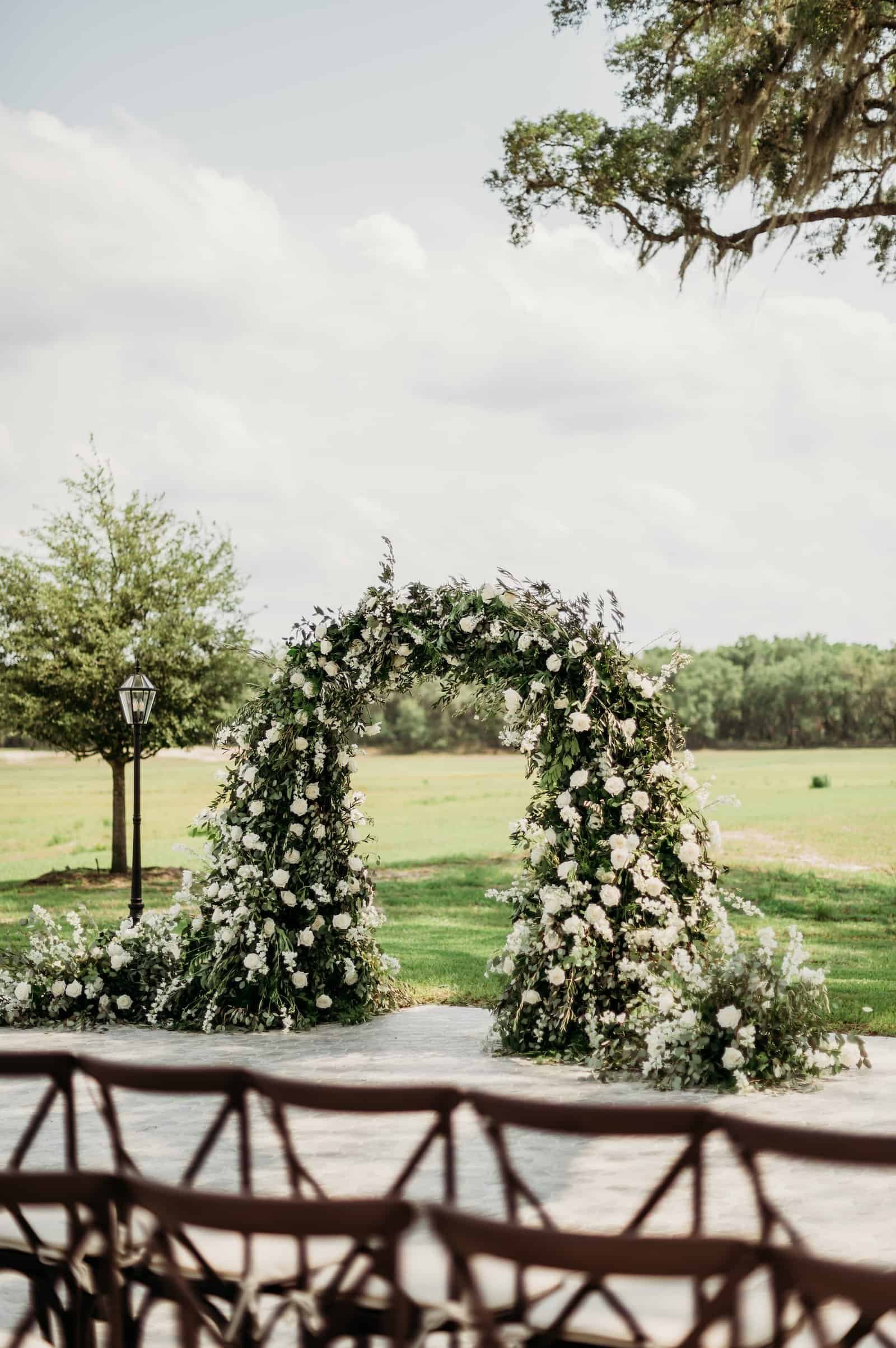 Lush Outdoor Lawn Ceremony at Pelican Golf Club Featuring Manicured Greens and a Verdant White Floral Arch