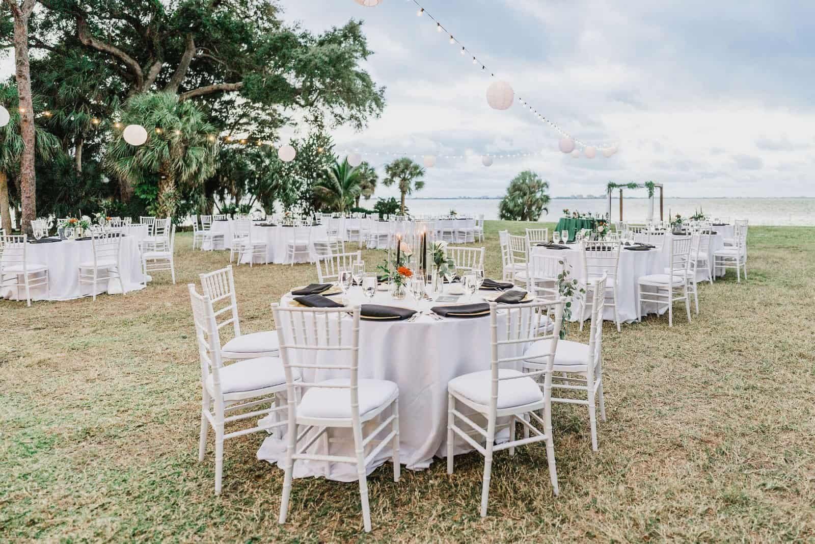 Round tables set on the bay lawn at the Powel Crosley Estate under globe string lights