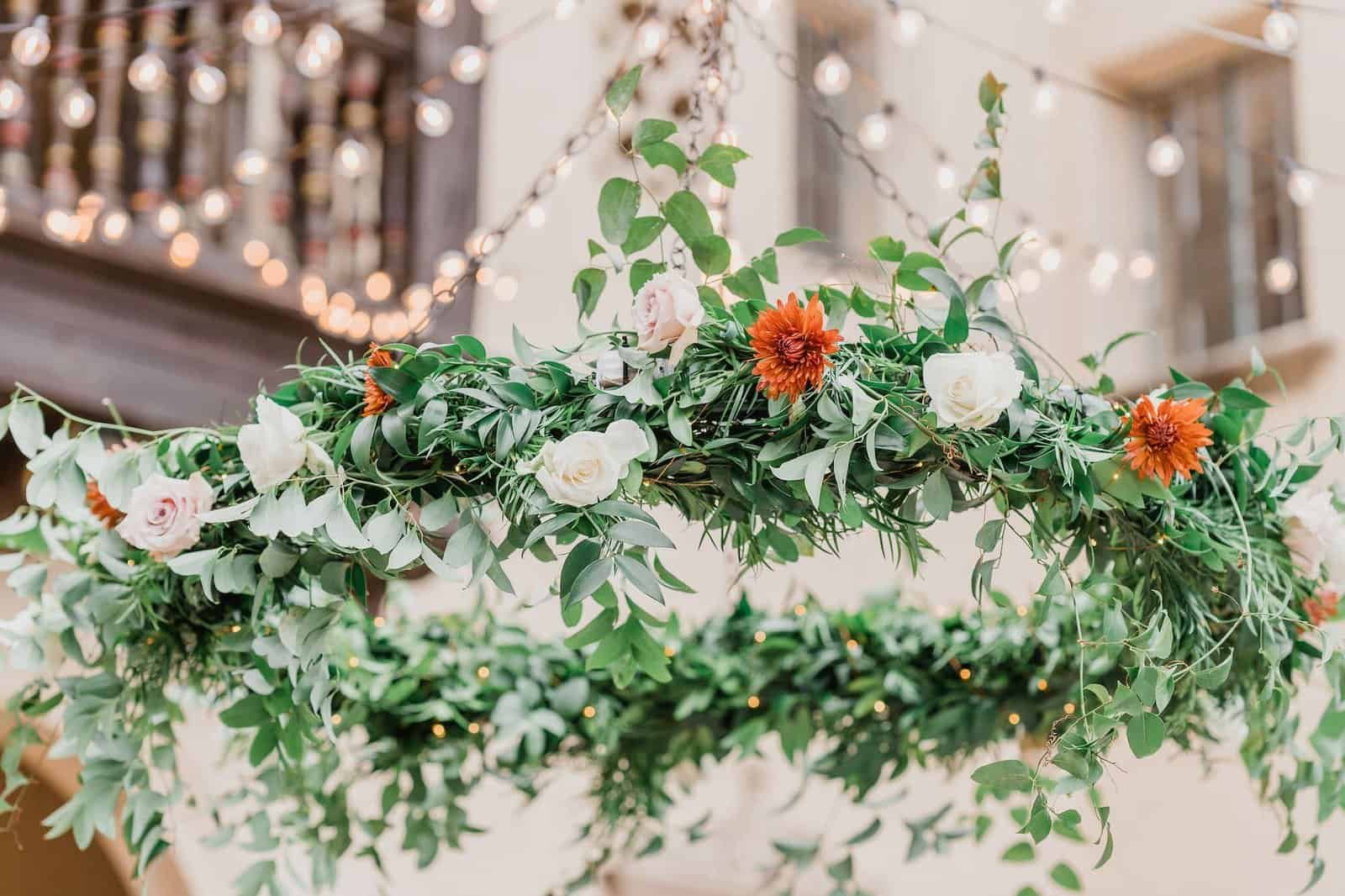 Hanging floral greenery chandelier with orange chrysanthemums and white roses over the patio dance floor