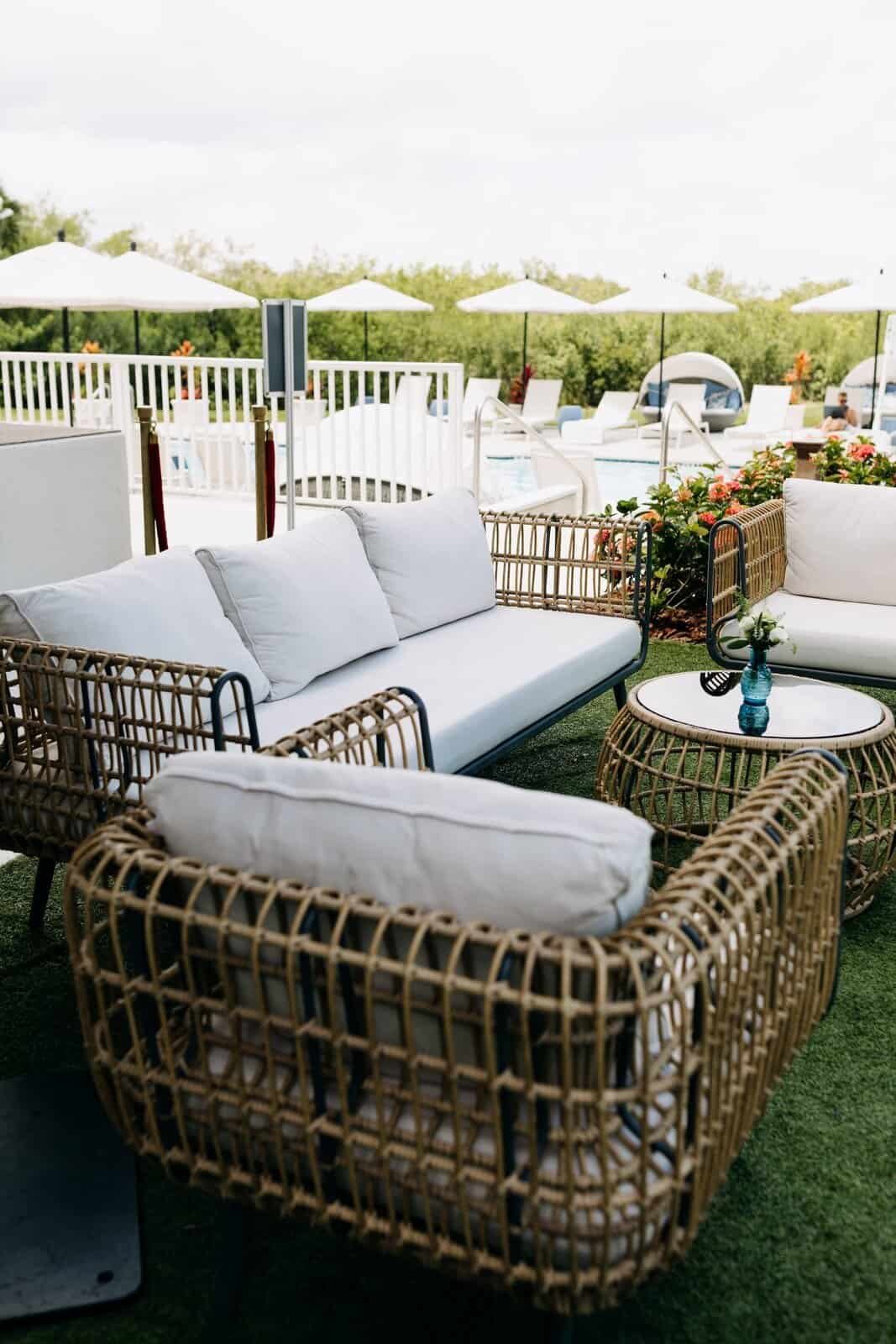 Rattan lounge furniture with white cushions and side tables set up on the lawn for cocktail hour