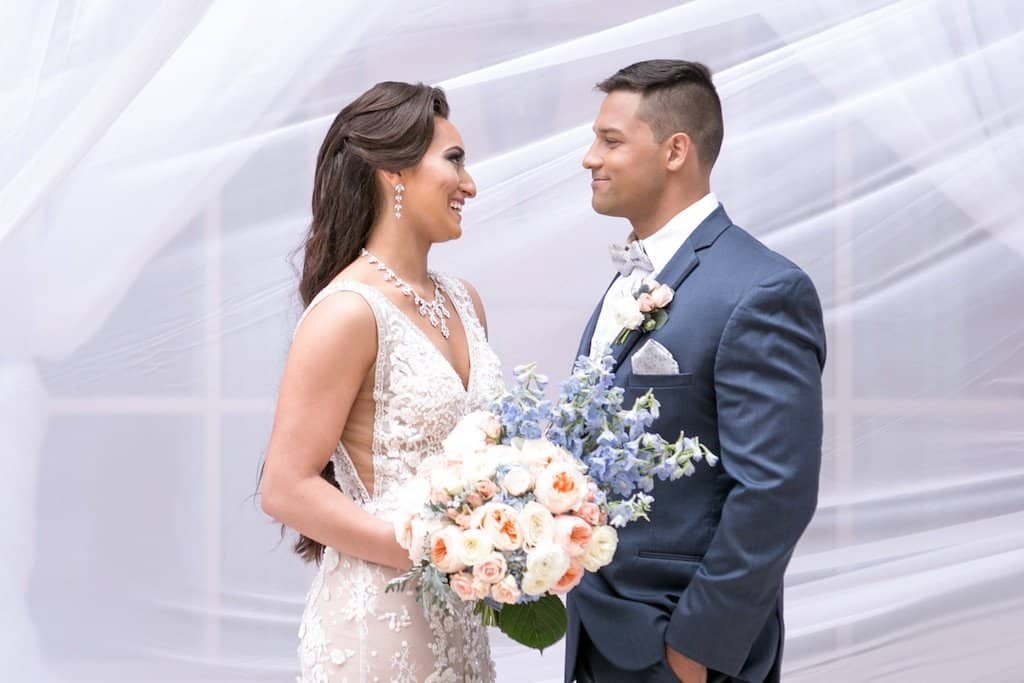 A romantic outdoor wedding ceremony setup featuring a draped arch and cross-back chairs.