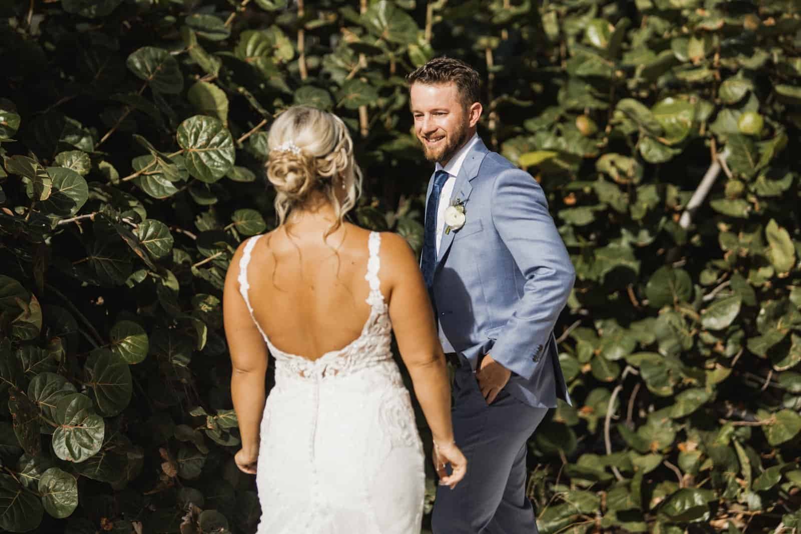 A circular floral arch stands on the white sand during a beach wedding.