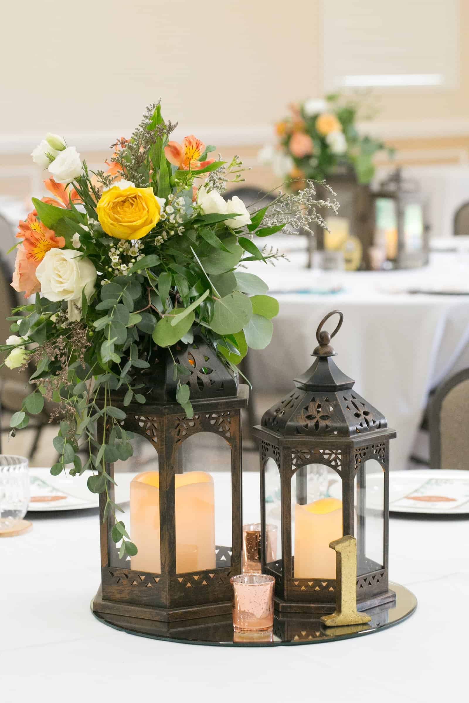 Round table centerpiece with circular mirror tray, matte black lanterns, glowing pillar candles, and blush rose blossoms