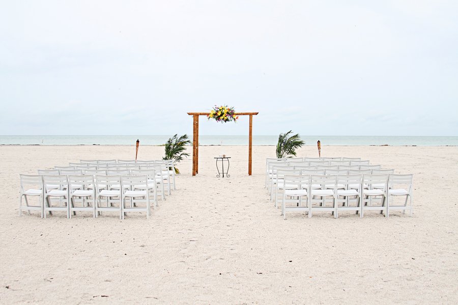 A romantic tented beach reception set up on the sand at sunset.