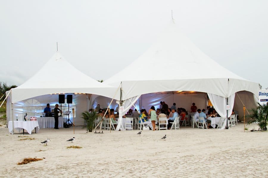 The happy couple smiling under umbrellas during their rainy beach wedding ceremony.