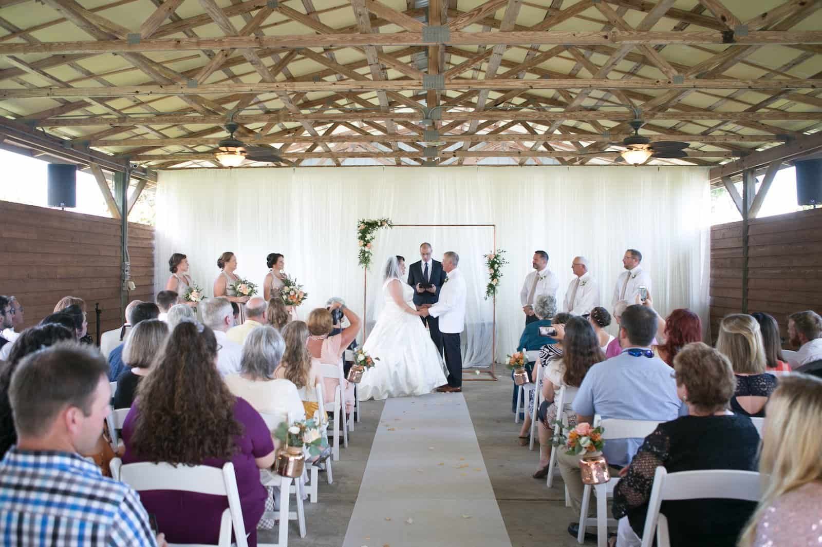 Sarah and Alan exchanging wedding vows under a handmade copper arbor adorned with fresh greenery and garden roses