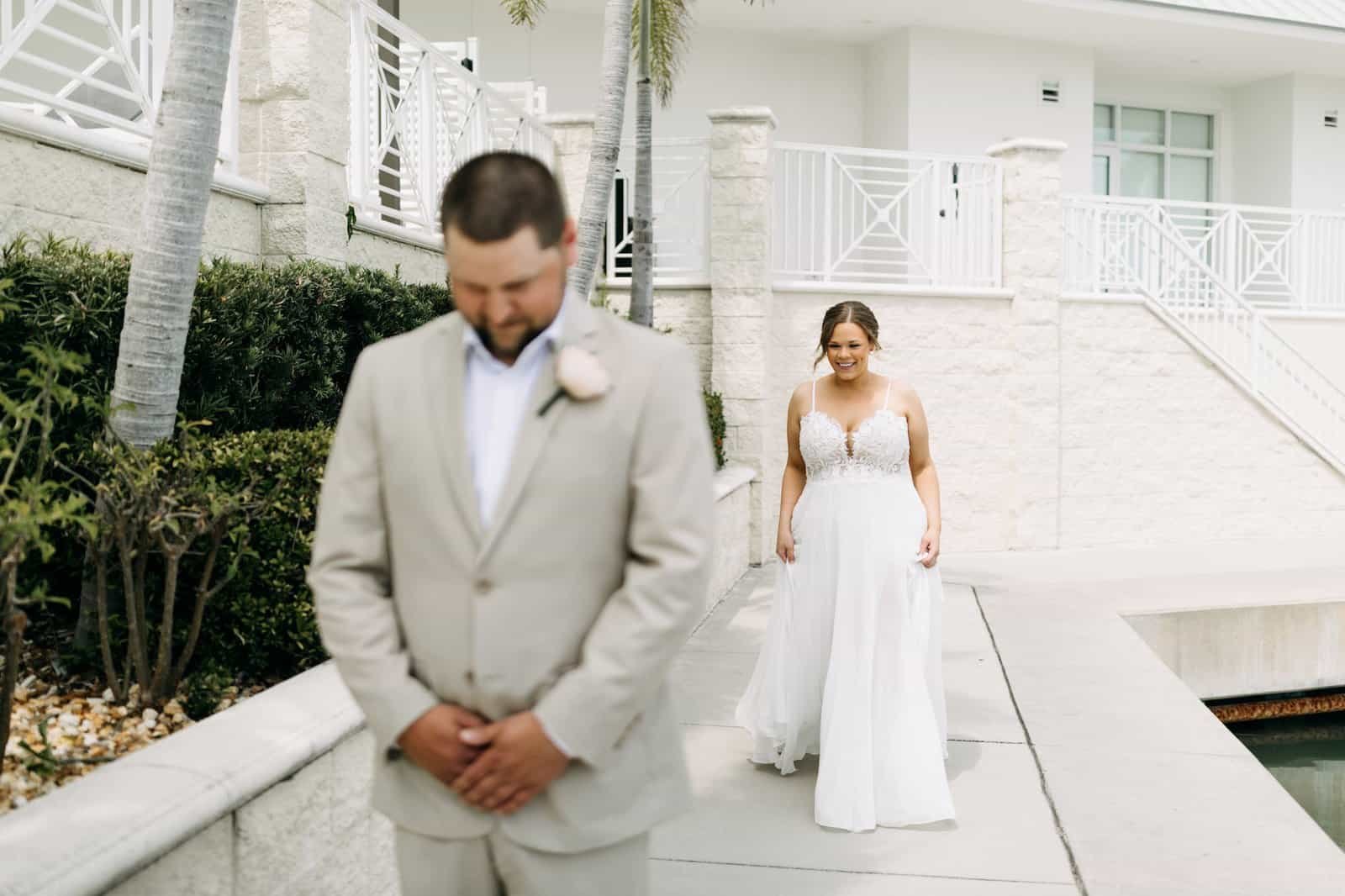 A bride and groom standing before a floral arch with waterfront views.