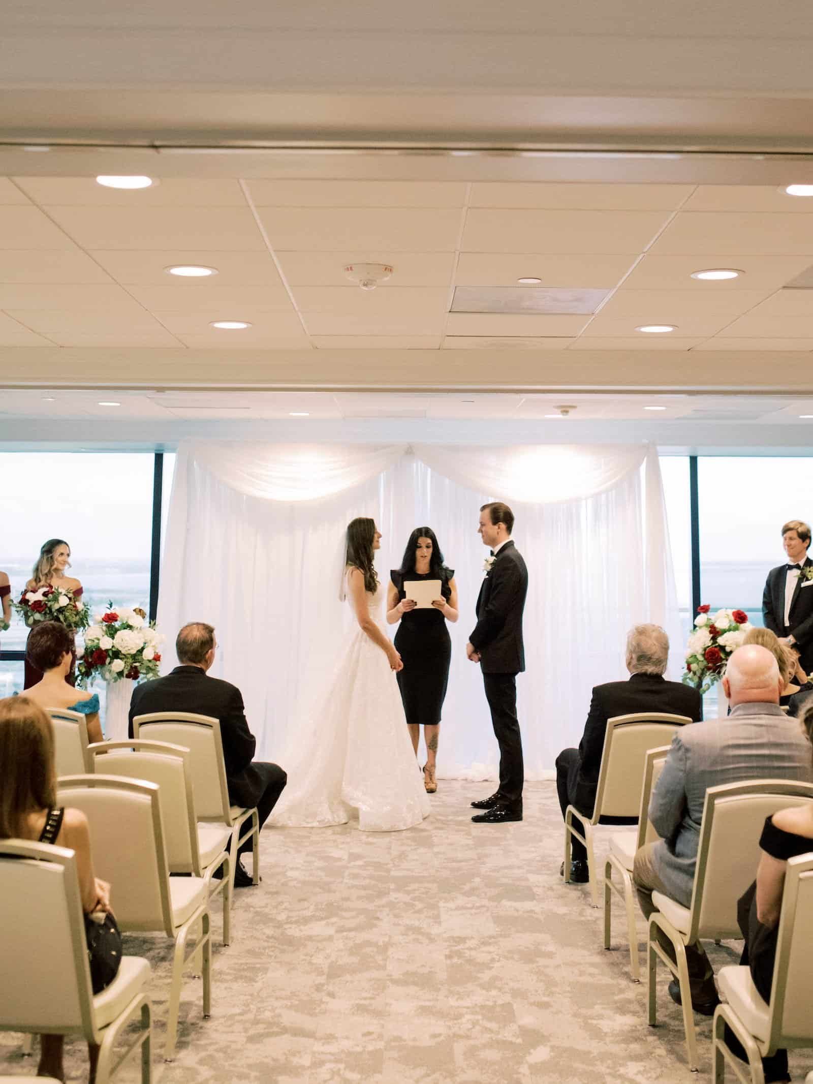 Indoor wedding ceremony at The Tampa Club with elegant pipe and drape backdrop and panoramic downtown Tampa skyline views