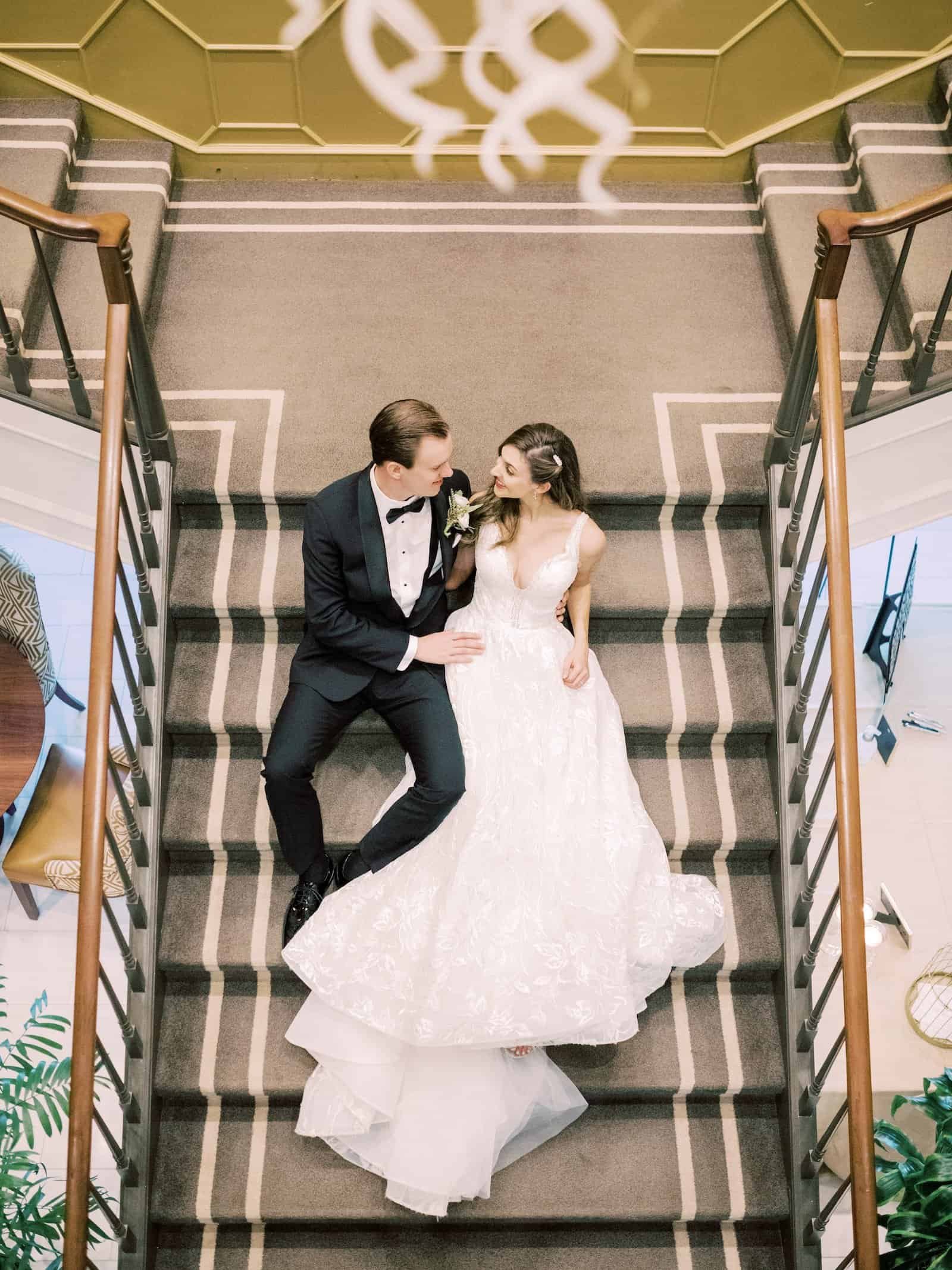 Bride in Allure Couture gown and groom in black tuxedo on The Tampa Club grand architectural staircase