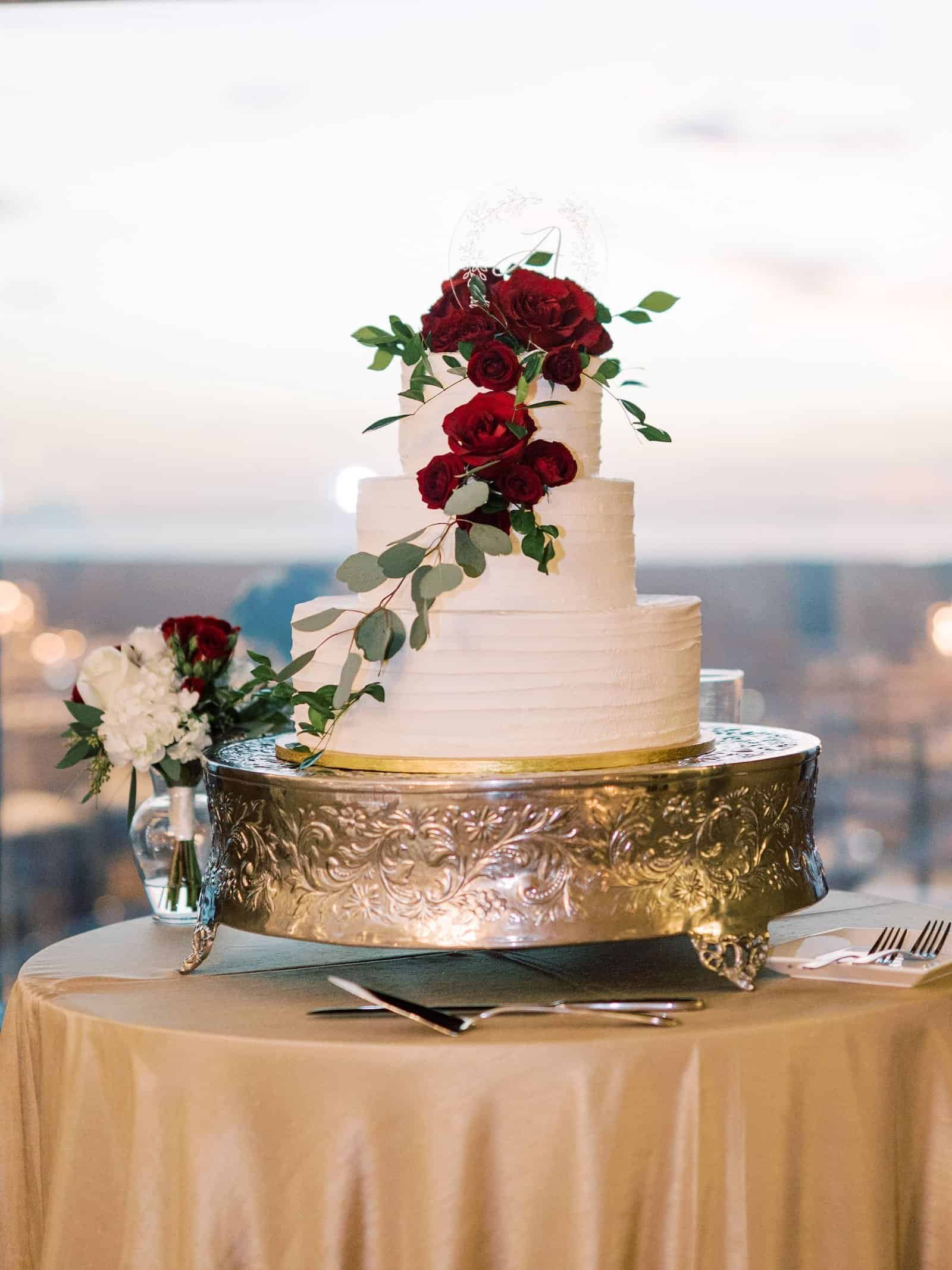 Three tier textured buttercream wedding cake adorned with fresh merlot roses on an ornate gold stand