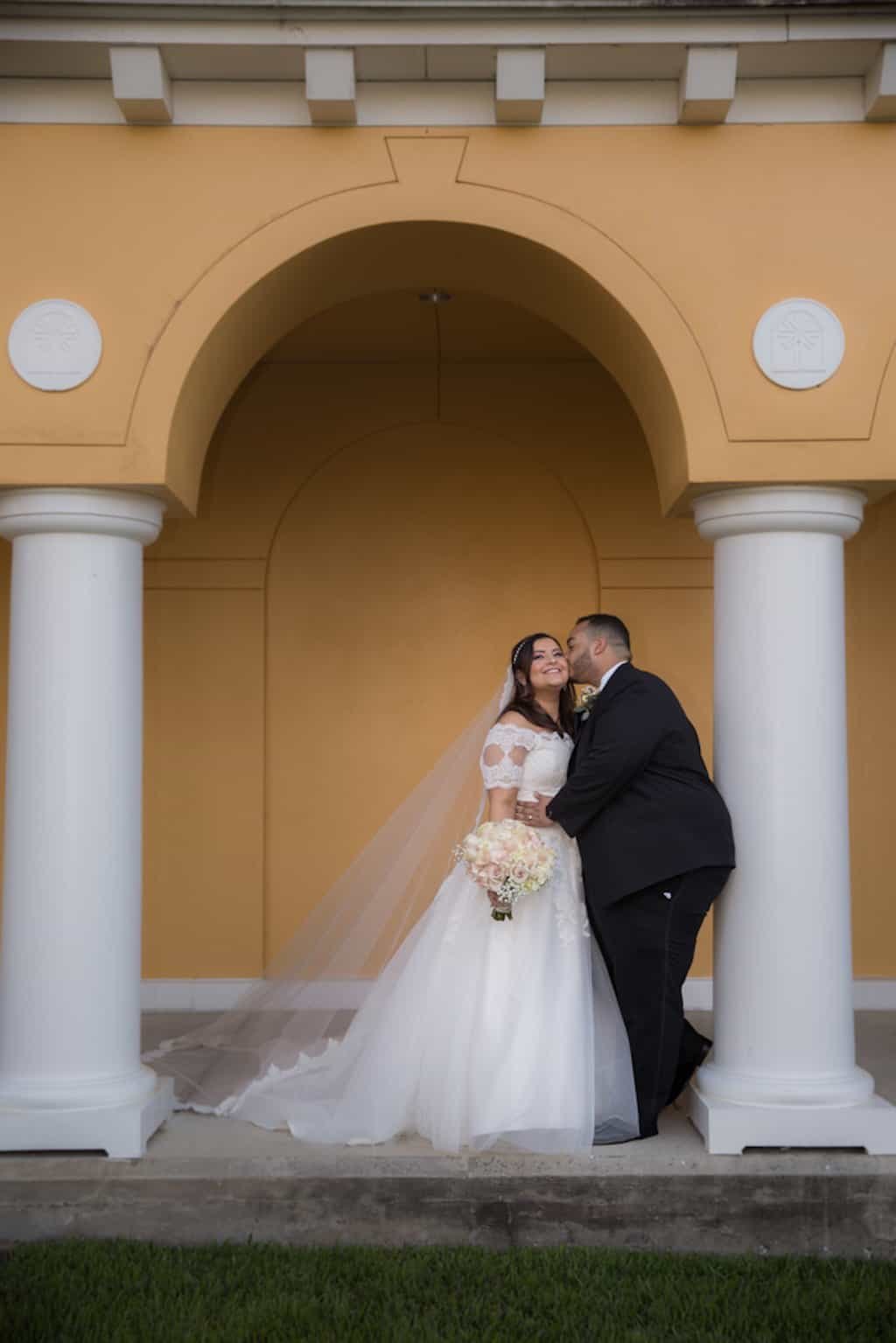 Bride in lace Pronovias gown and groom in classic black suit holding bouquet on the outdoor veranda at Tampa Palms