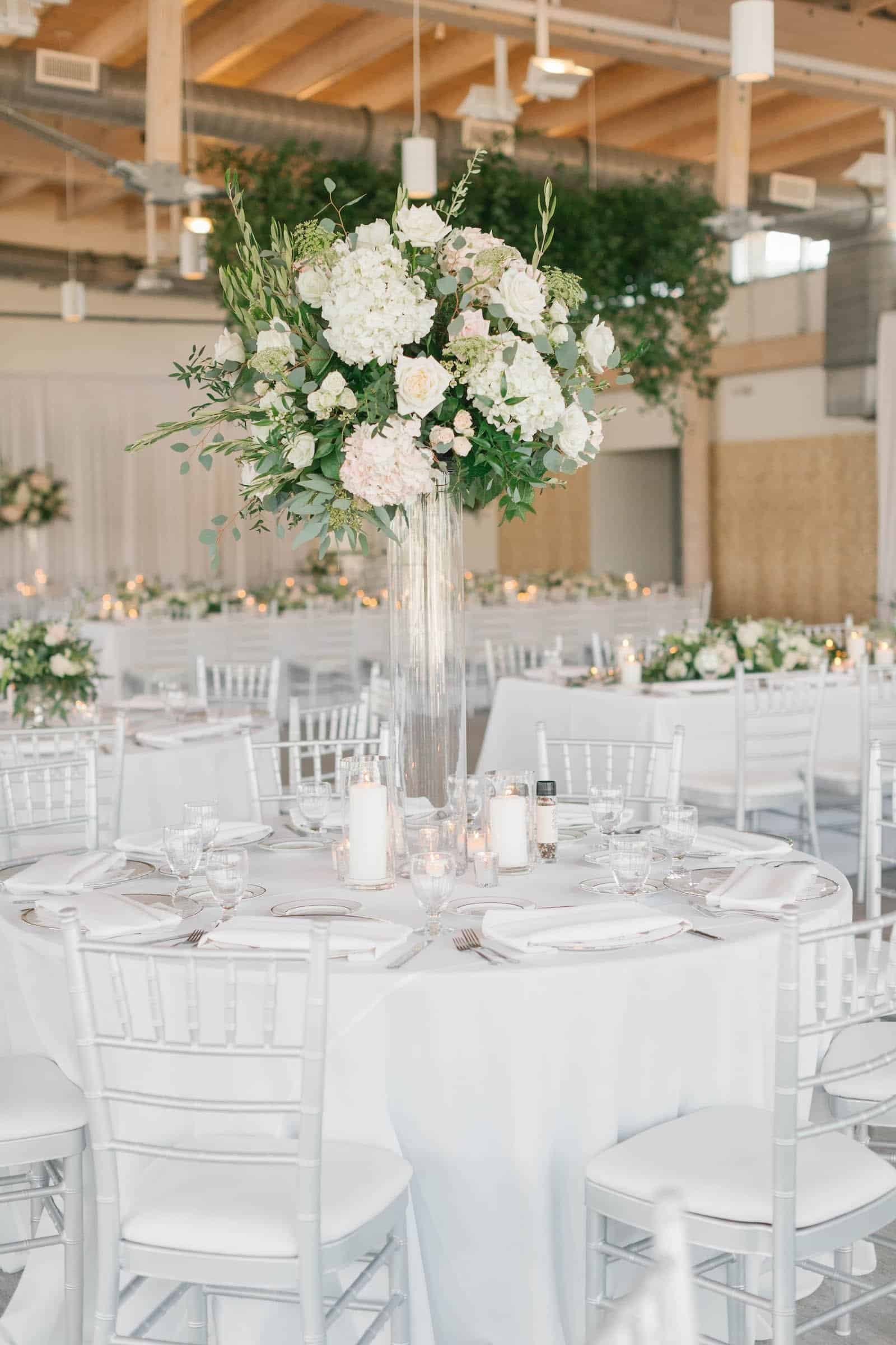 Contemporary reception table featuring lush greenery centerpieces and glowing candles at night.