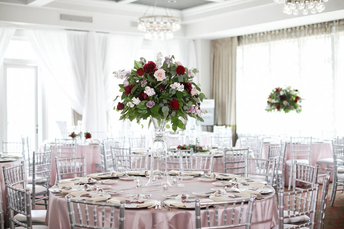 Luxury wedding reception tablescape with dusty rose linens, silver chiavari chairs, and tall floral centerpieces