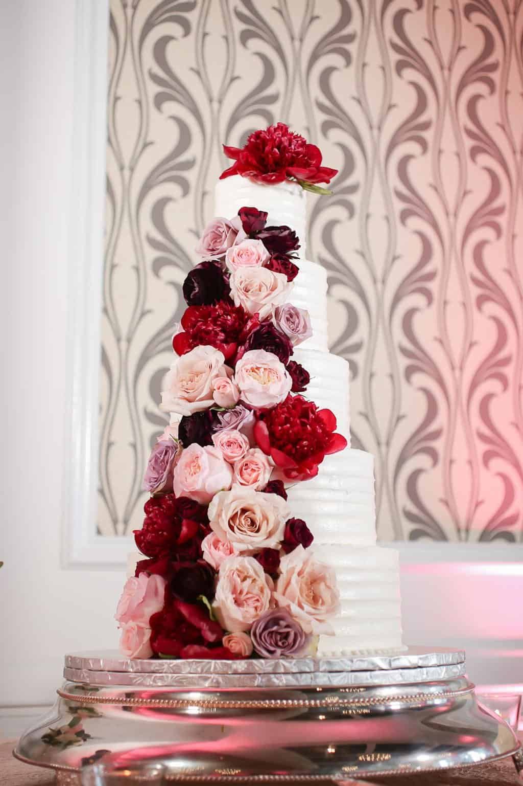 Five-tier white wedding cake with cascading dusty rose and wine red garden roses at The Birchwood