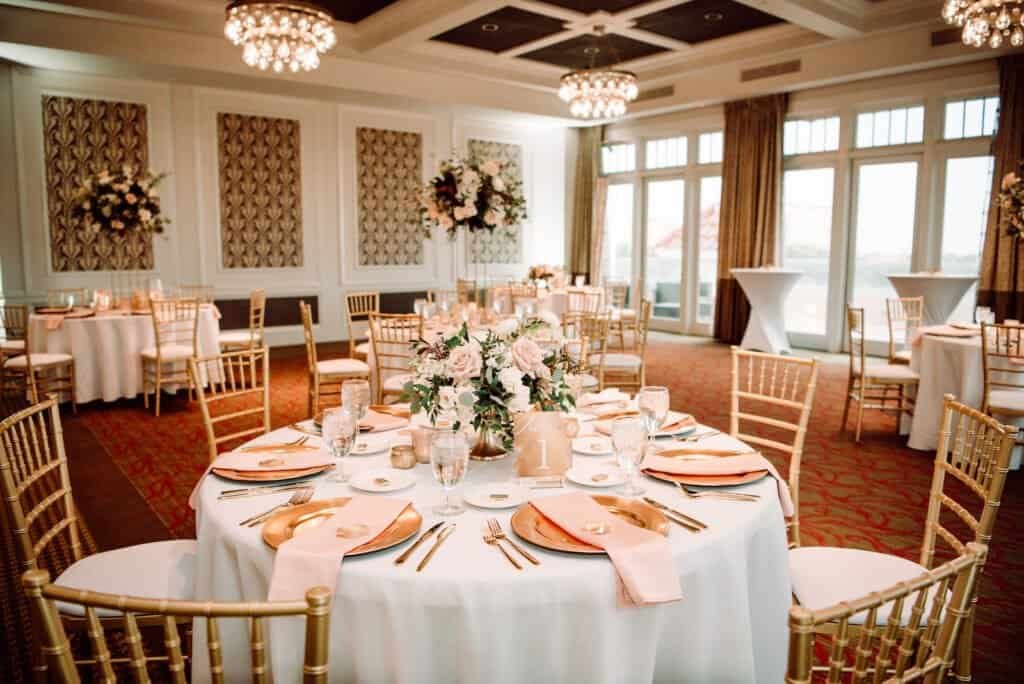 Reception at The Birchwood with round tables in ivory linen and gold Chiavari chairs under the ballroom chandeliers