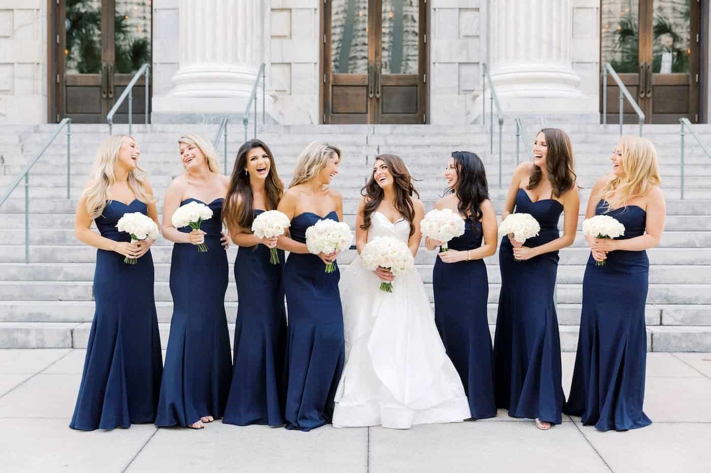 Bridesmaids in sophisticated midnight blue gowns posing during a romantic Tampa waterfront wedding celebration.