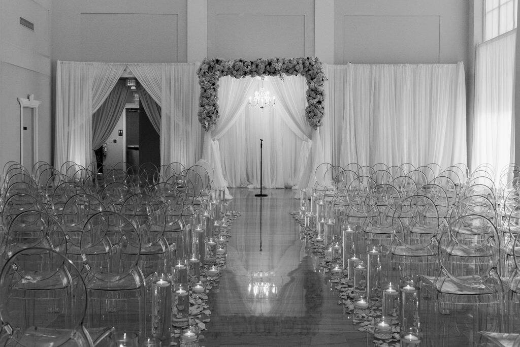 Ceremony Setup at The Vault with Clear Ghost Chairs Floating Candle Cylinders and Crystal Chandelier by Gabro Event Services
