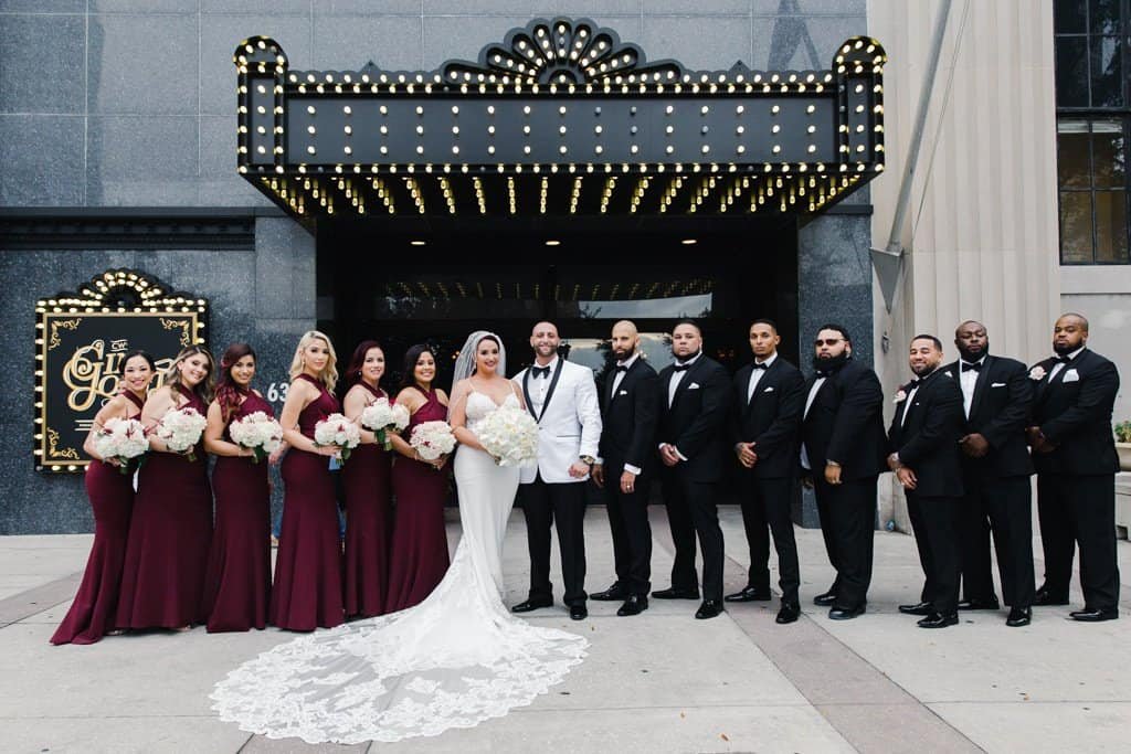 Full Wedding Party with Bridesmaids in Maroon Gowns and Groomsmen in Classic Black Tuxedos