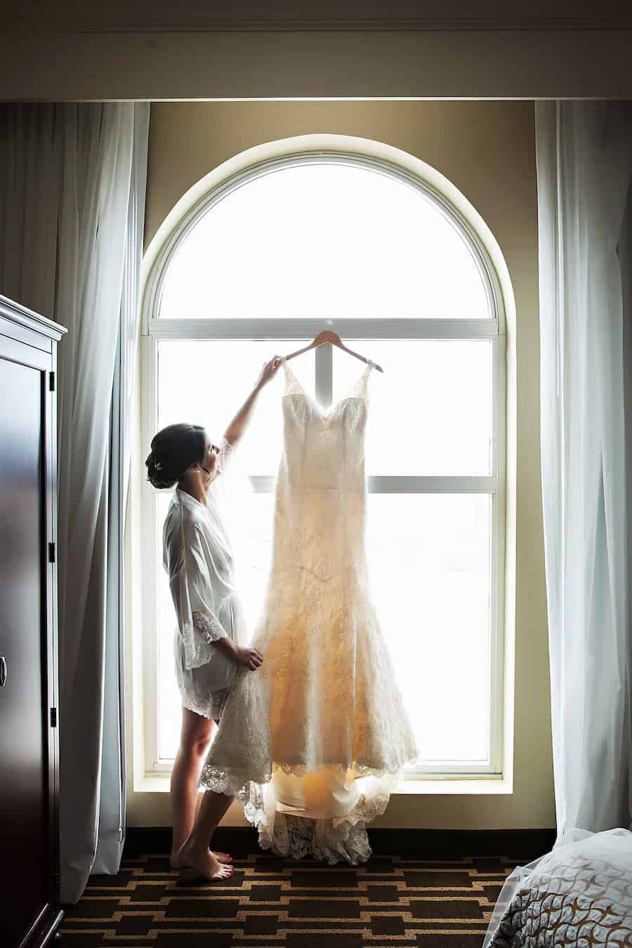 Four-tiered classic white wedding cake with gold ribbon trim displayed in front of custom sheer wall draping