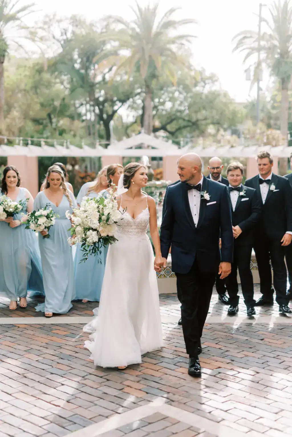 Bride and groom with bridal party in mismatching pastel blue Revelry dresses and black tuxedos at The Vinoy