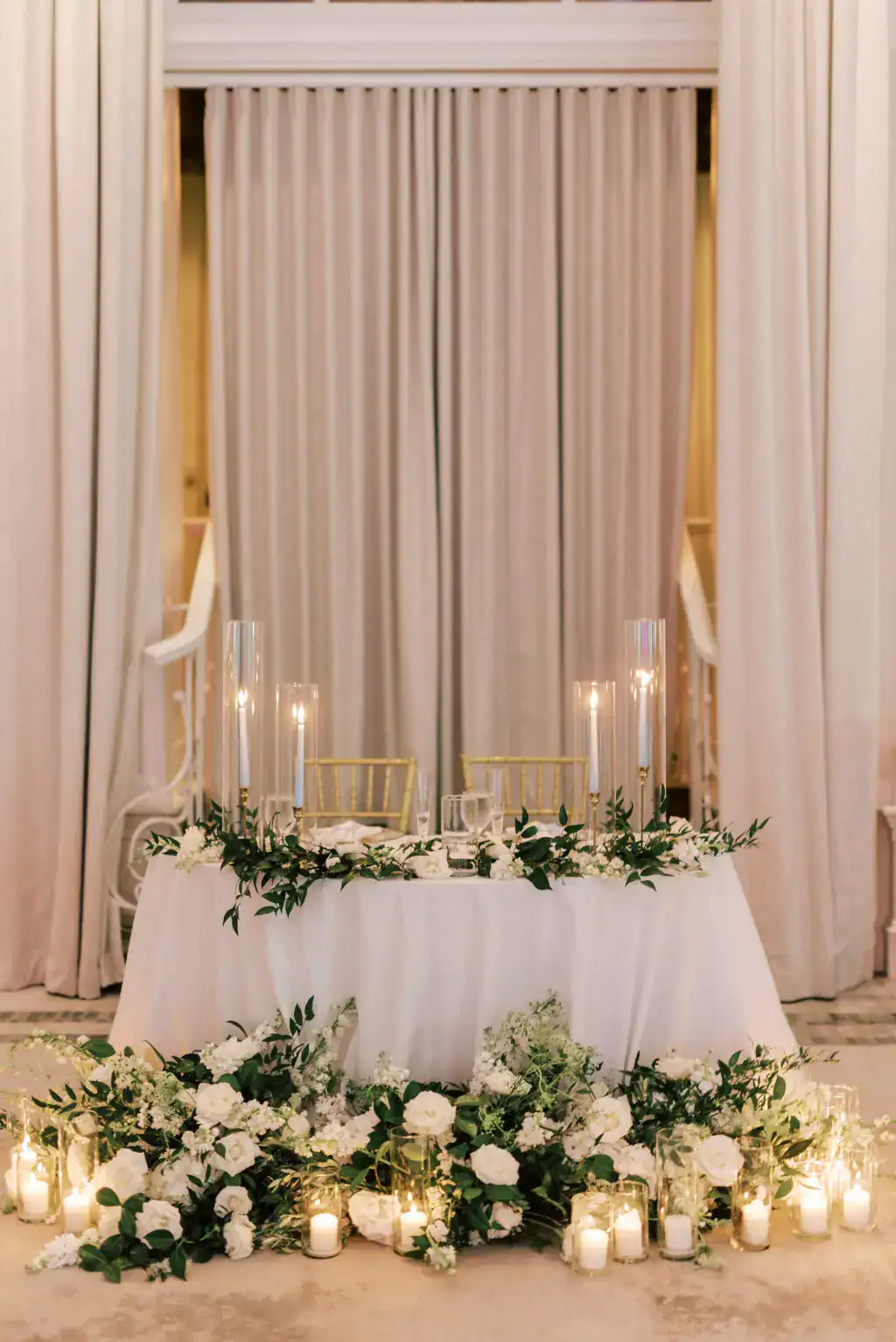 Romantic candlelit sweetheart table wedding reception decor with white roses and greenery